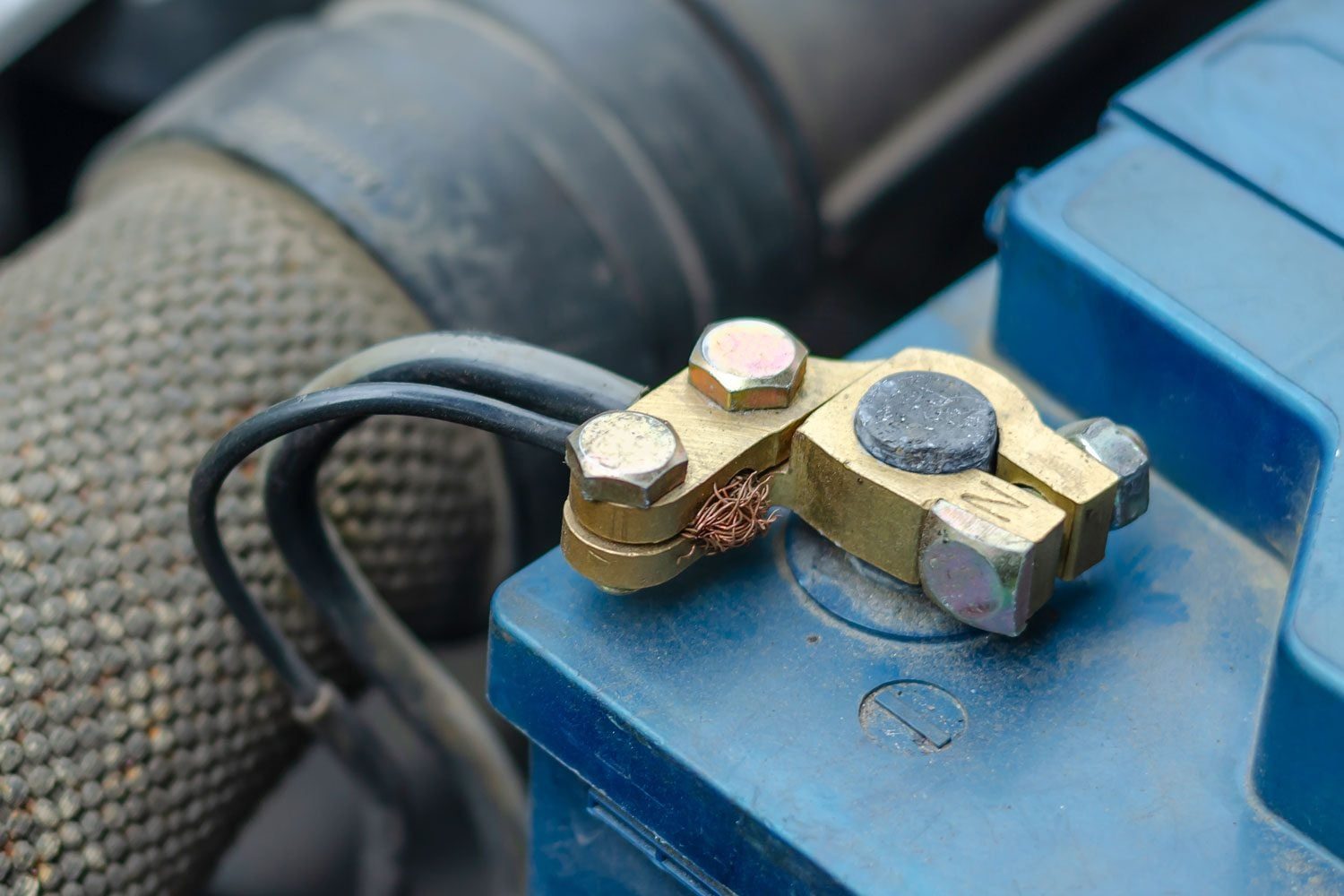 A brass battery terminal connects wires, while a nearby copper strand rests on the surface. The setting appears to be under the hood of a ve