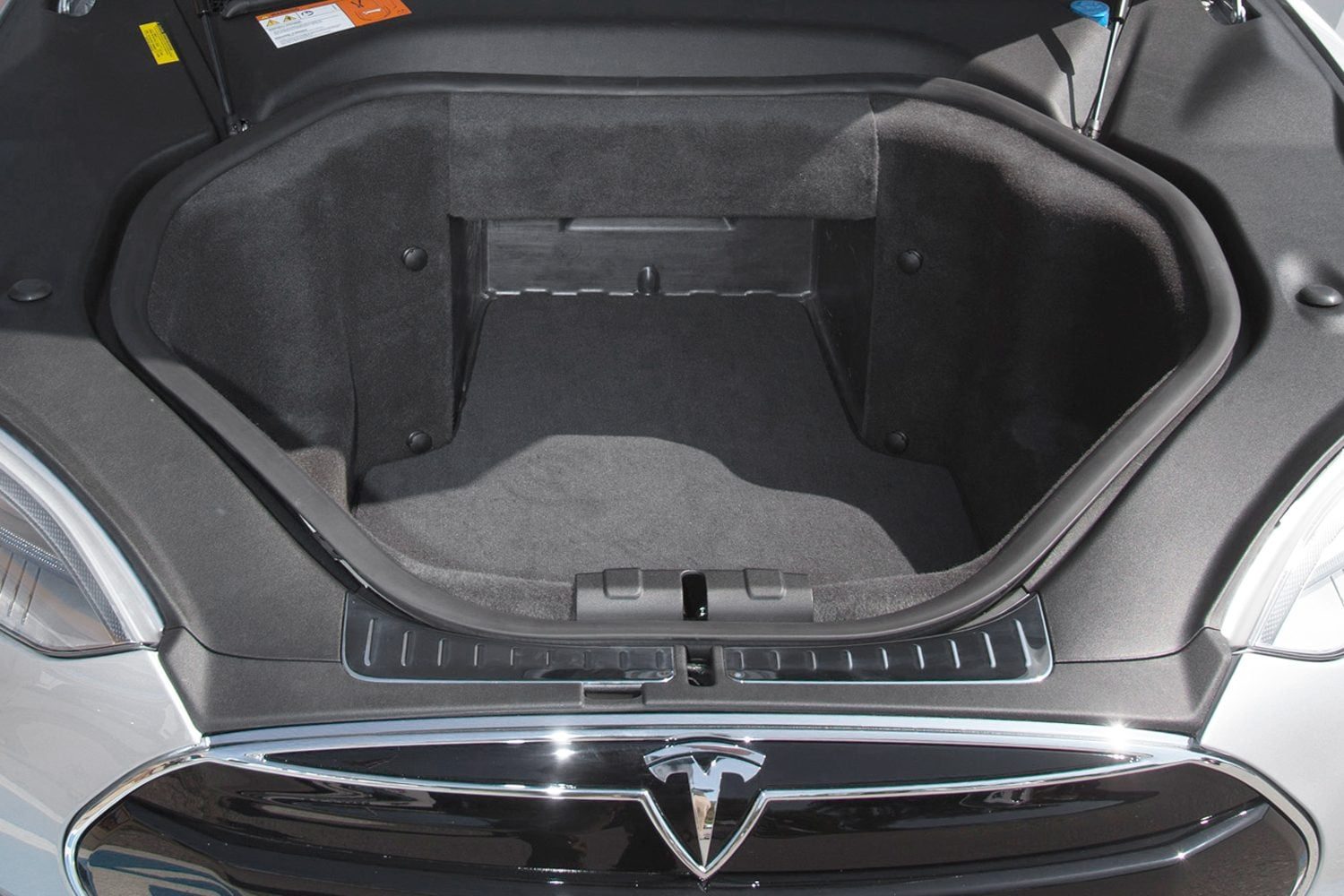 An empty car frunk showcases a spacious, black, carpeted storage area with smooth edges, surrounded by the vehicle's metallic front and slee