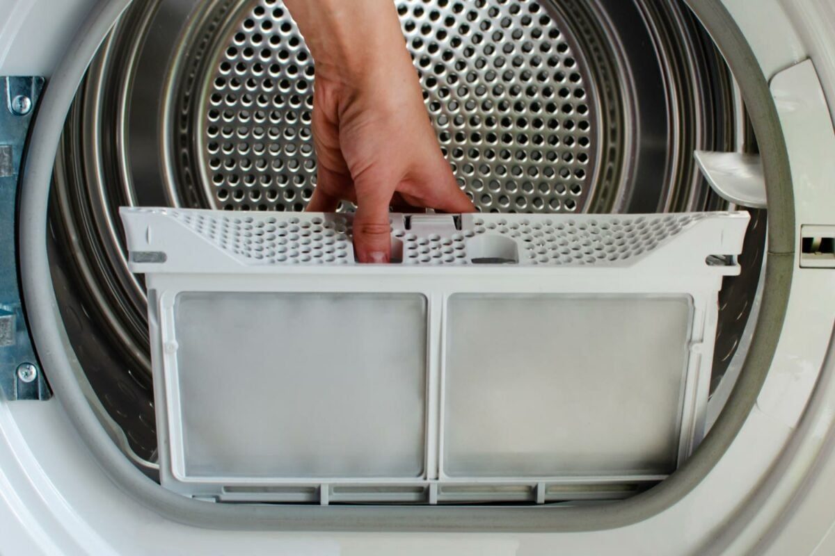 A hand inserts a white lint filter into a dryer, surrounded by a metallic drum with a perforated design, indicating its operational environm