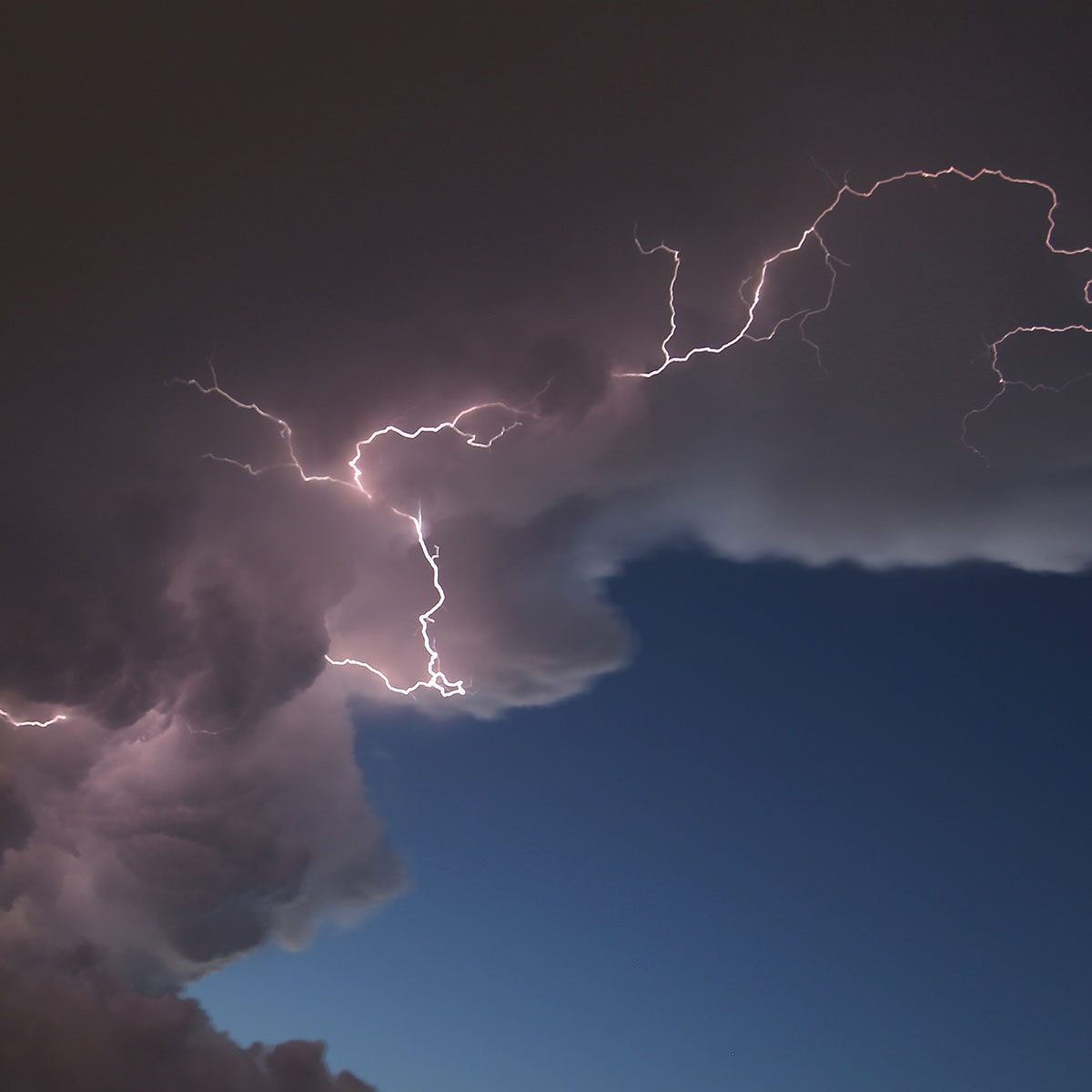 Lightning strikes through dark clouds, illuminating the sky, while a lighter blue horizon hints at an approaching storm or clearing weather.
