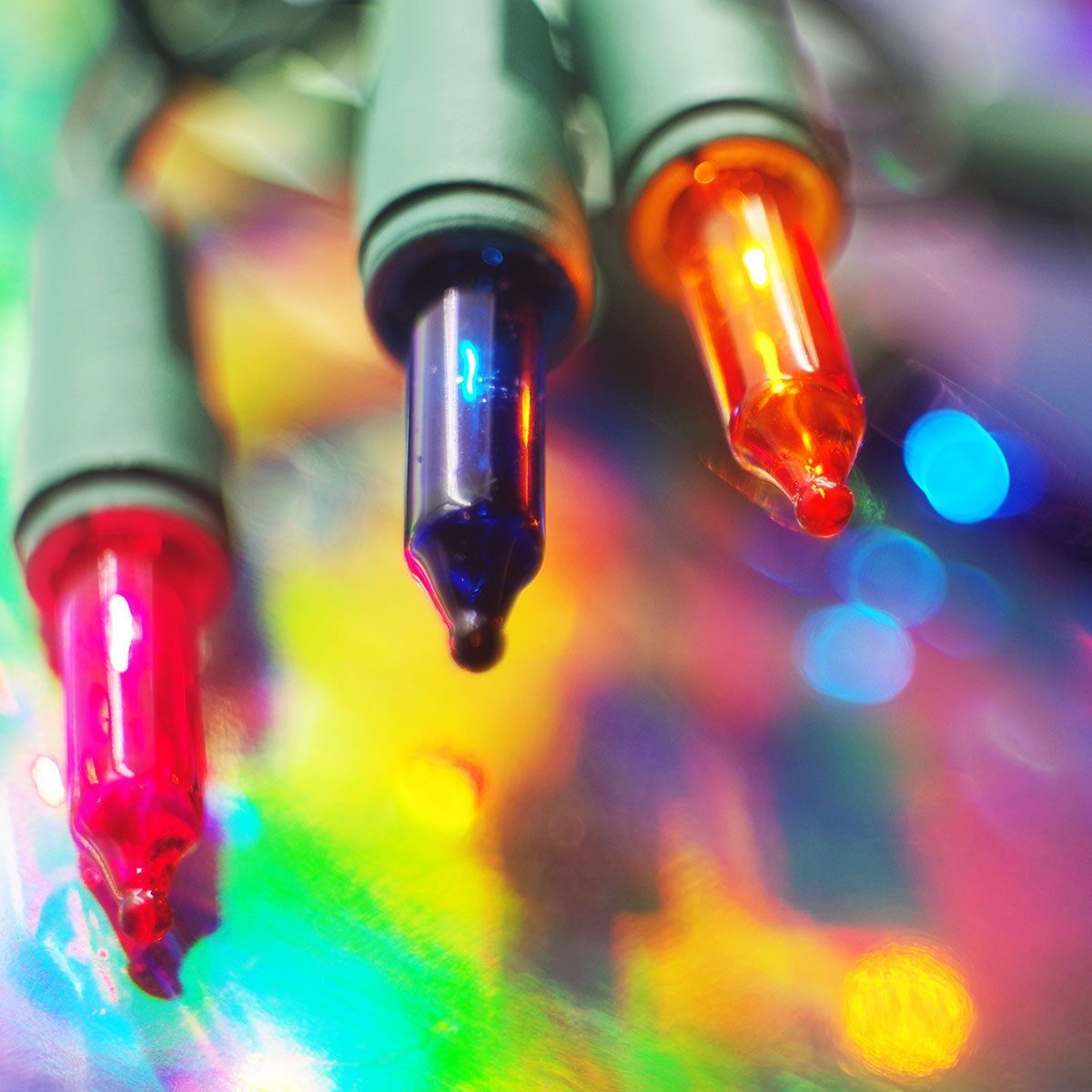Colored Christmas lights glow brightly, casting reflections on a shiny, multi-colored surface illuminated by additional blurred light source