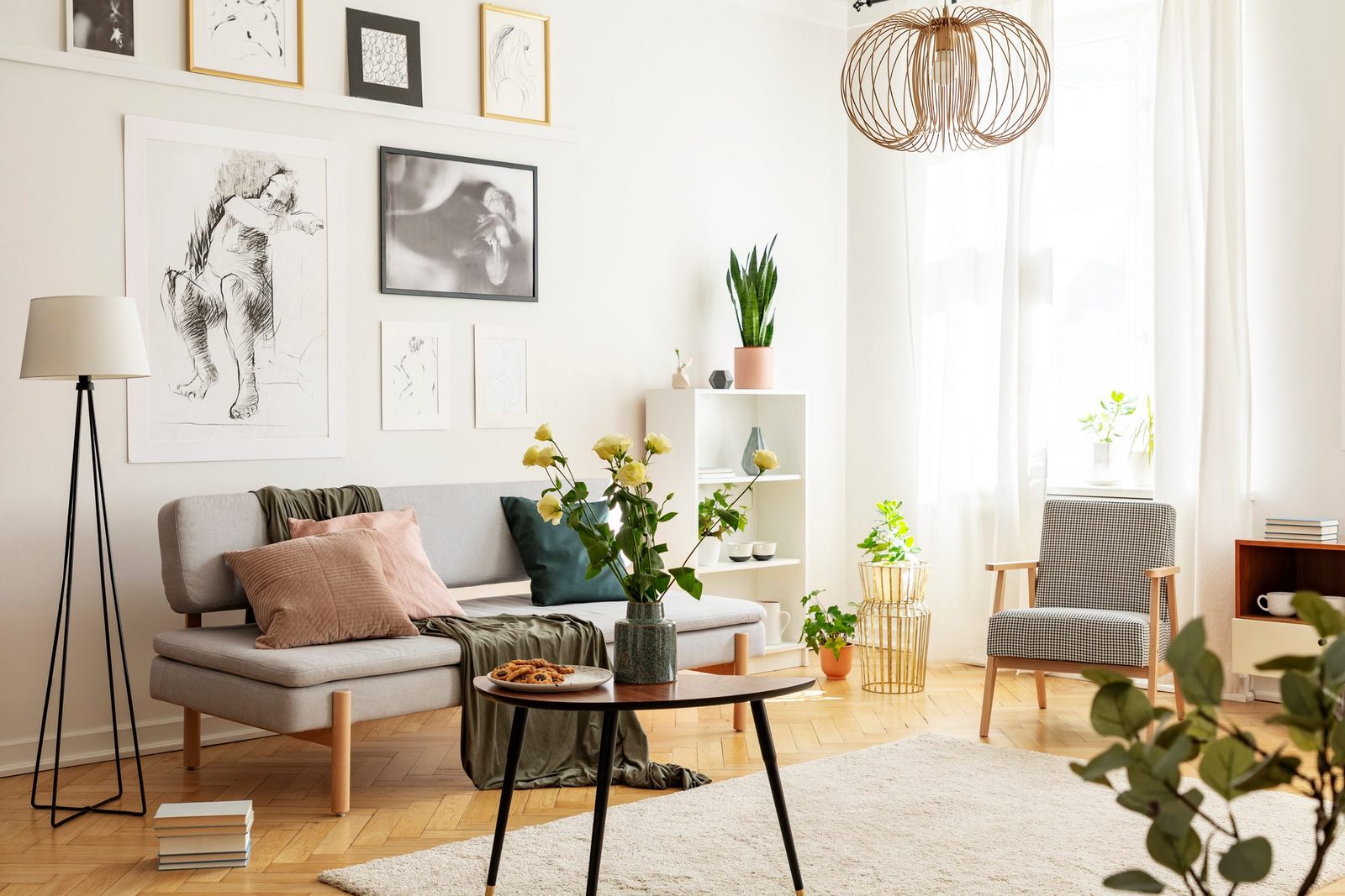 Flowers on wooden table next to grey couch in living room interior with lamp and posters. Real photo