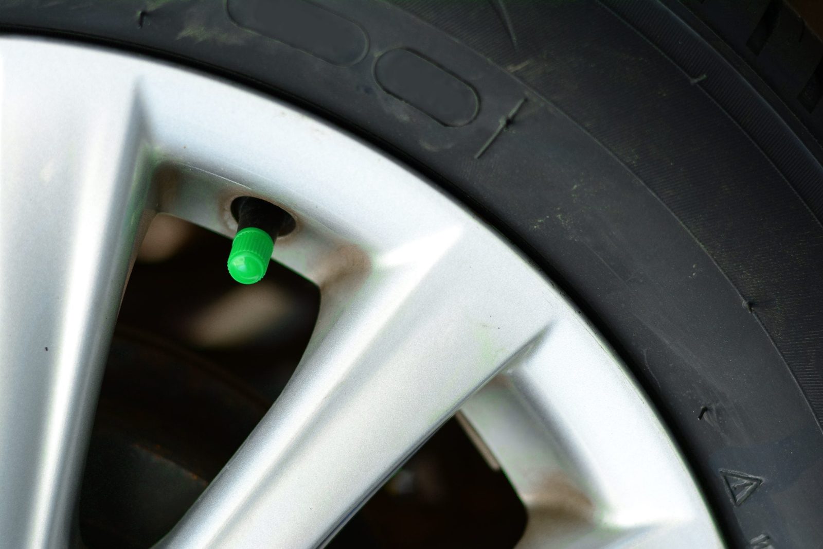 the green cover of tyre pressure valve on metal wheel with black tyre