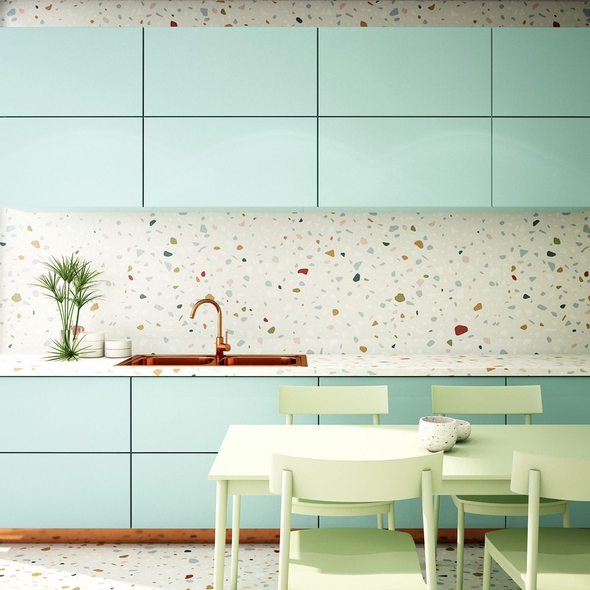 A mint green kitchen features a copper sink and countertop, surrounded by colorful speckled walls, with a matching table and chairs. A small