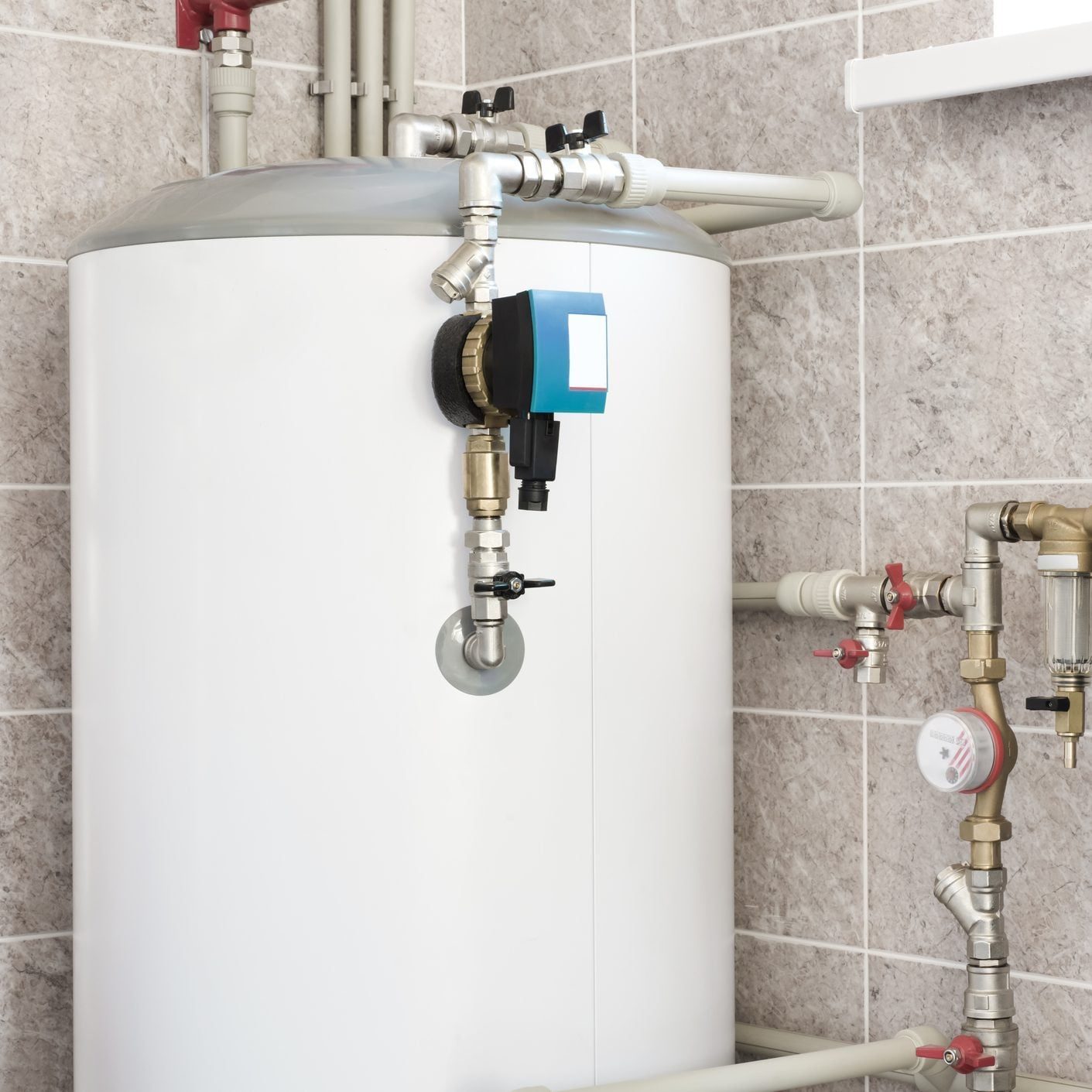 A water heater stands against a tiled wall, connected to various pipes and valves, indicating its role in managing hot water supply.