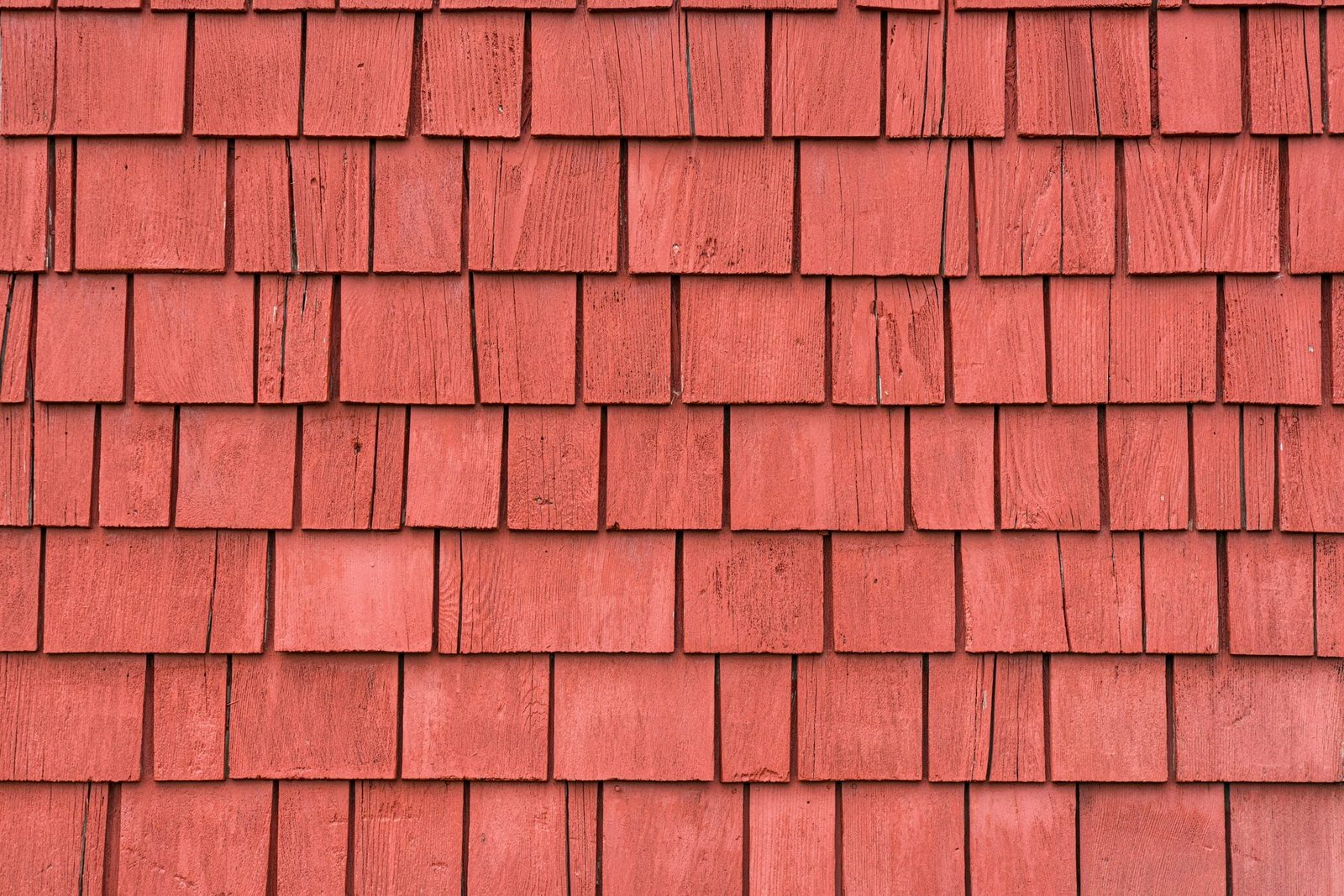 Wooden shingles cover a wall, arranged in overlapping rows. Their reddish hue suggests weatherproofing and adds a rustic aesthetic to the ar