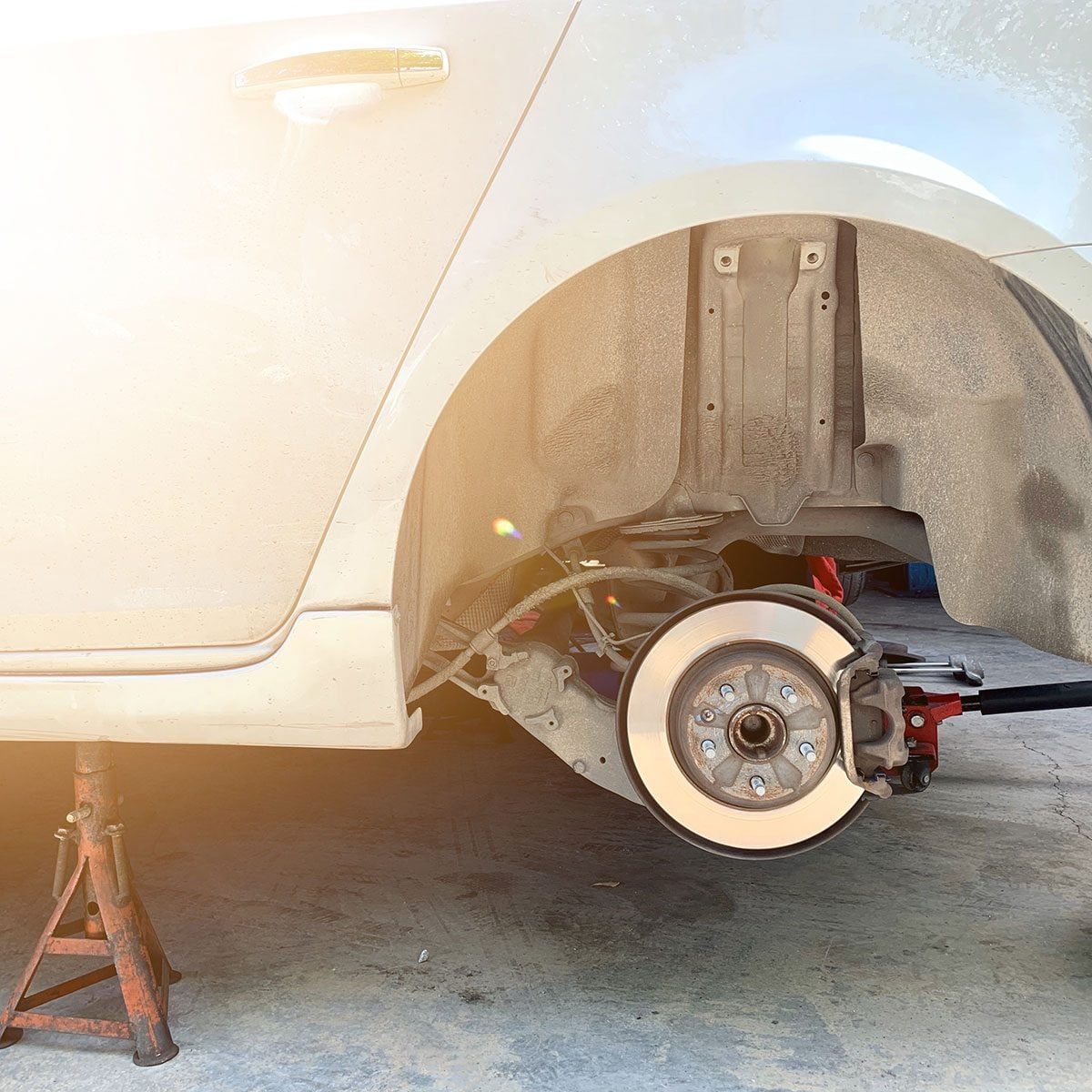 A car is lifted on a jack, displaying a removed wheel, while the environment appears dusty and sunlit.