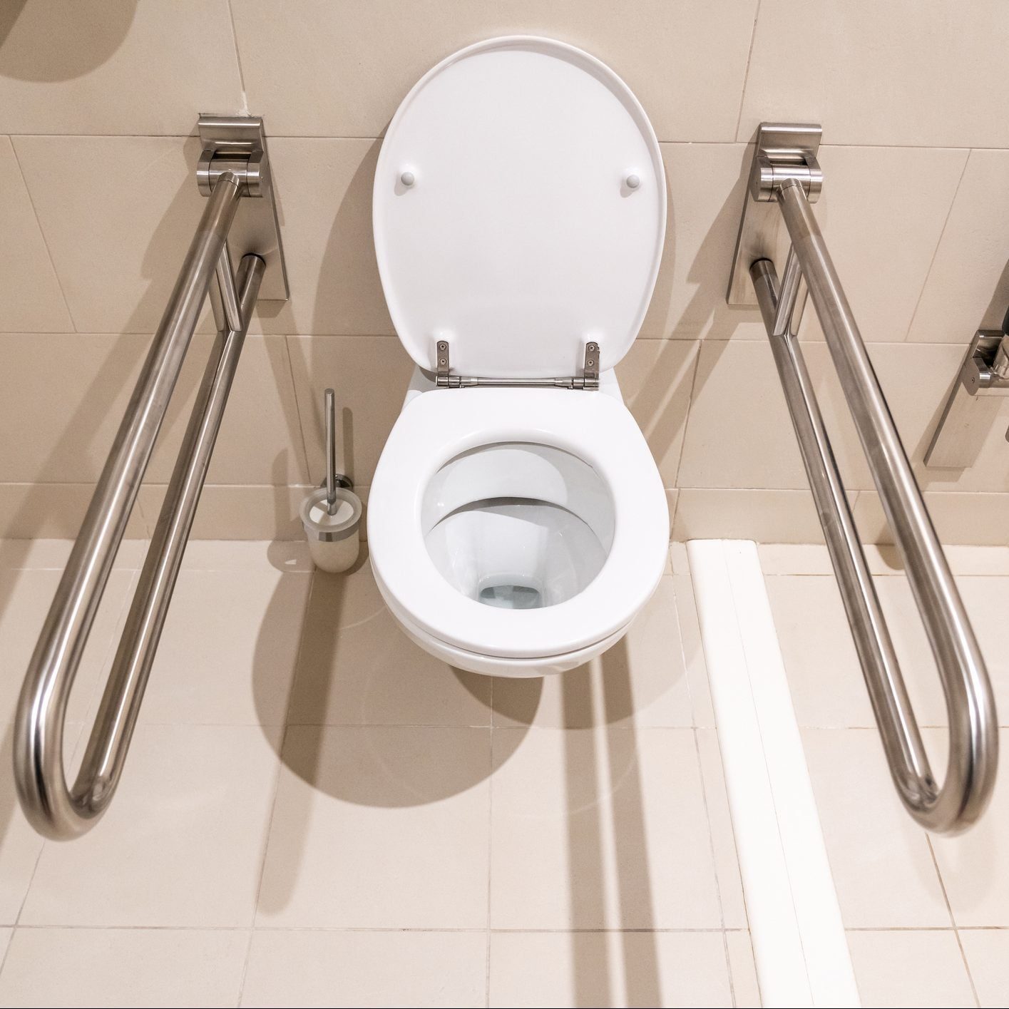 A white toilet with a raised lid is secured between two stainless steel grab bars, situated on tiled flooring in a restroom environment.