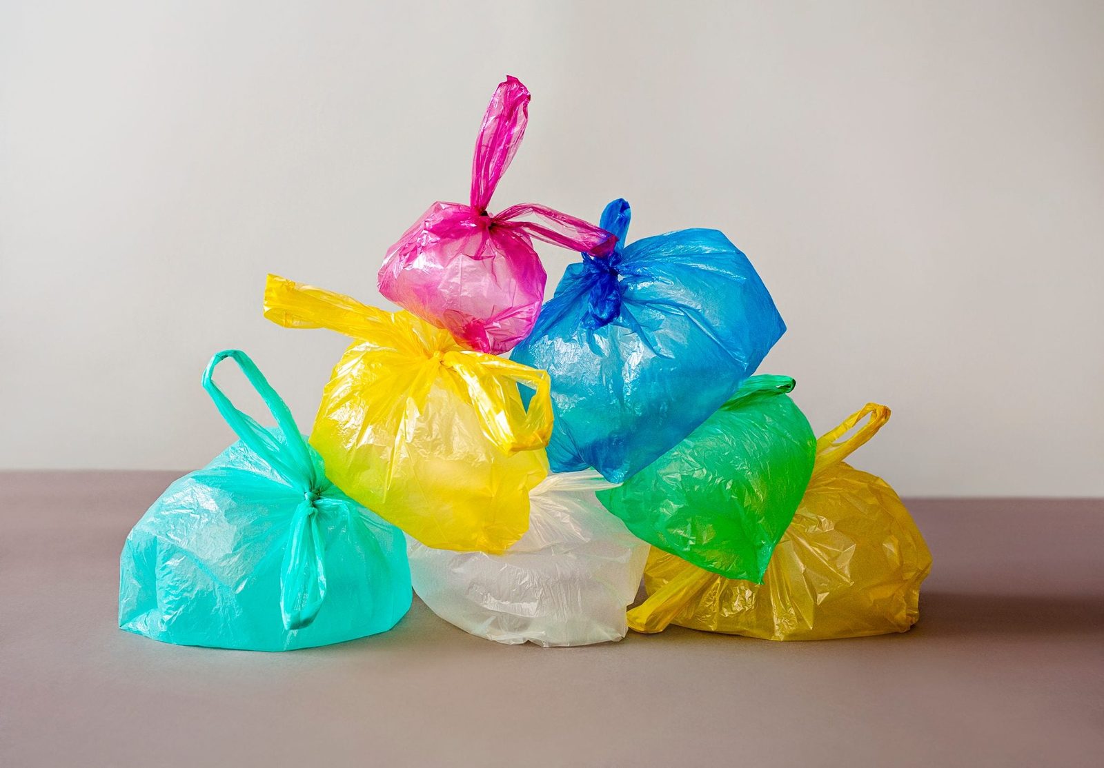 Colorful plastic bags are stacked together, creating a pile on a flat surface, against a softly lit, neutral background.