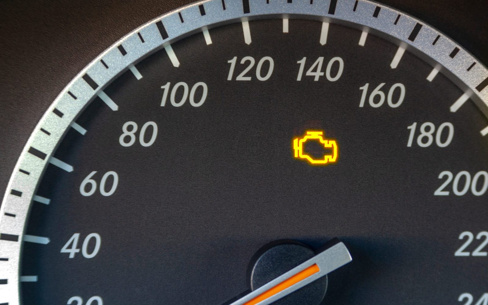 A vehicle dashboard displays a speedometer with an illuminated engine warning light on the right, indicating a potential issue with the engi