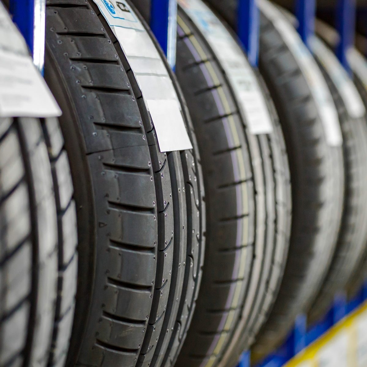 Rows of tires are displayed on metal racks, showcasing their tread patterns and labels, in a well-lit automotive shop environment.