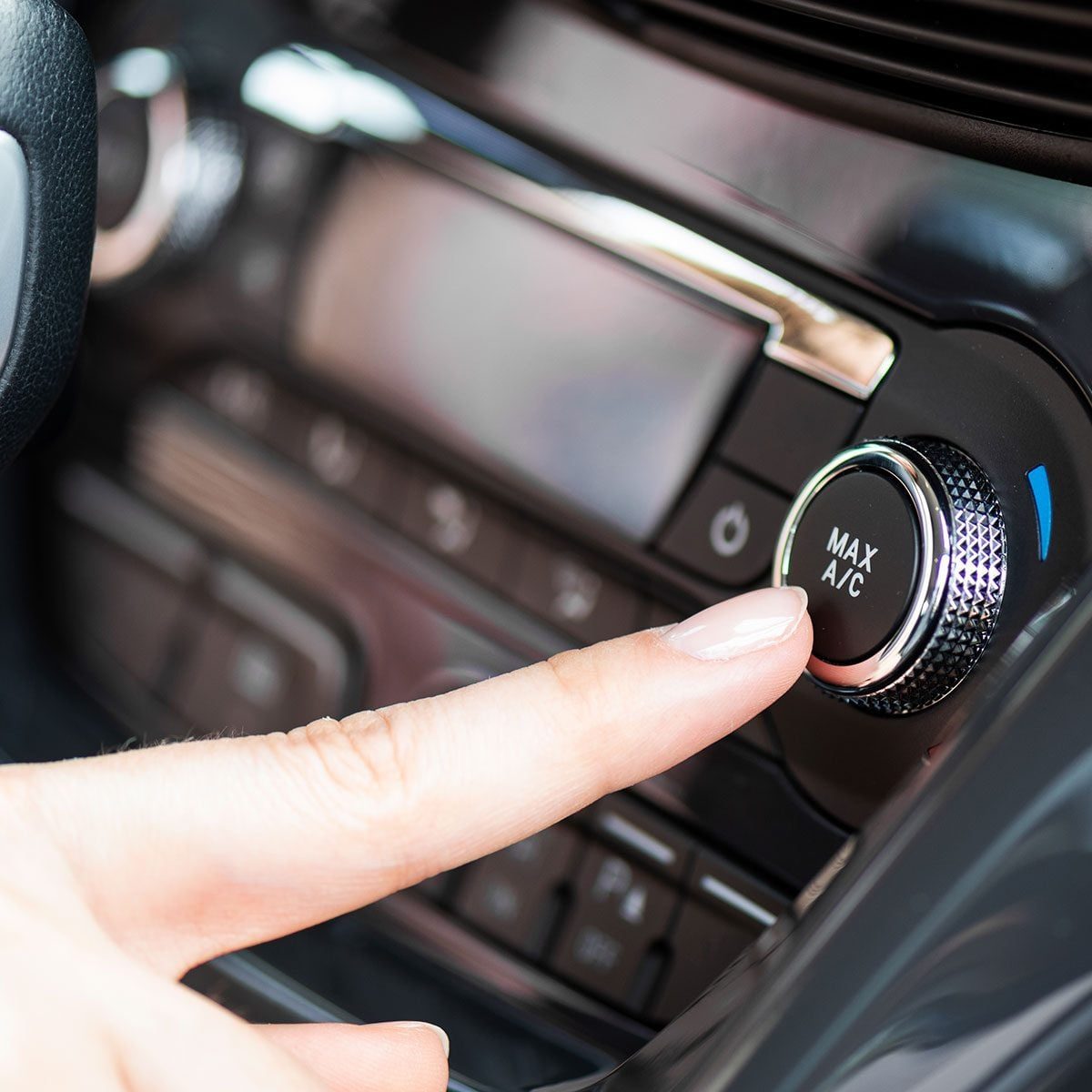 A hand presses the MAX A/C button on a car's dashboard, activating the air conditioning system in a vehicle's interior.