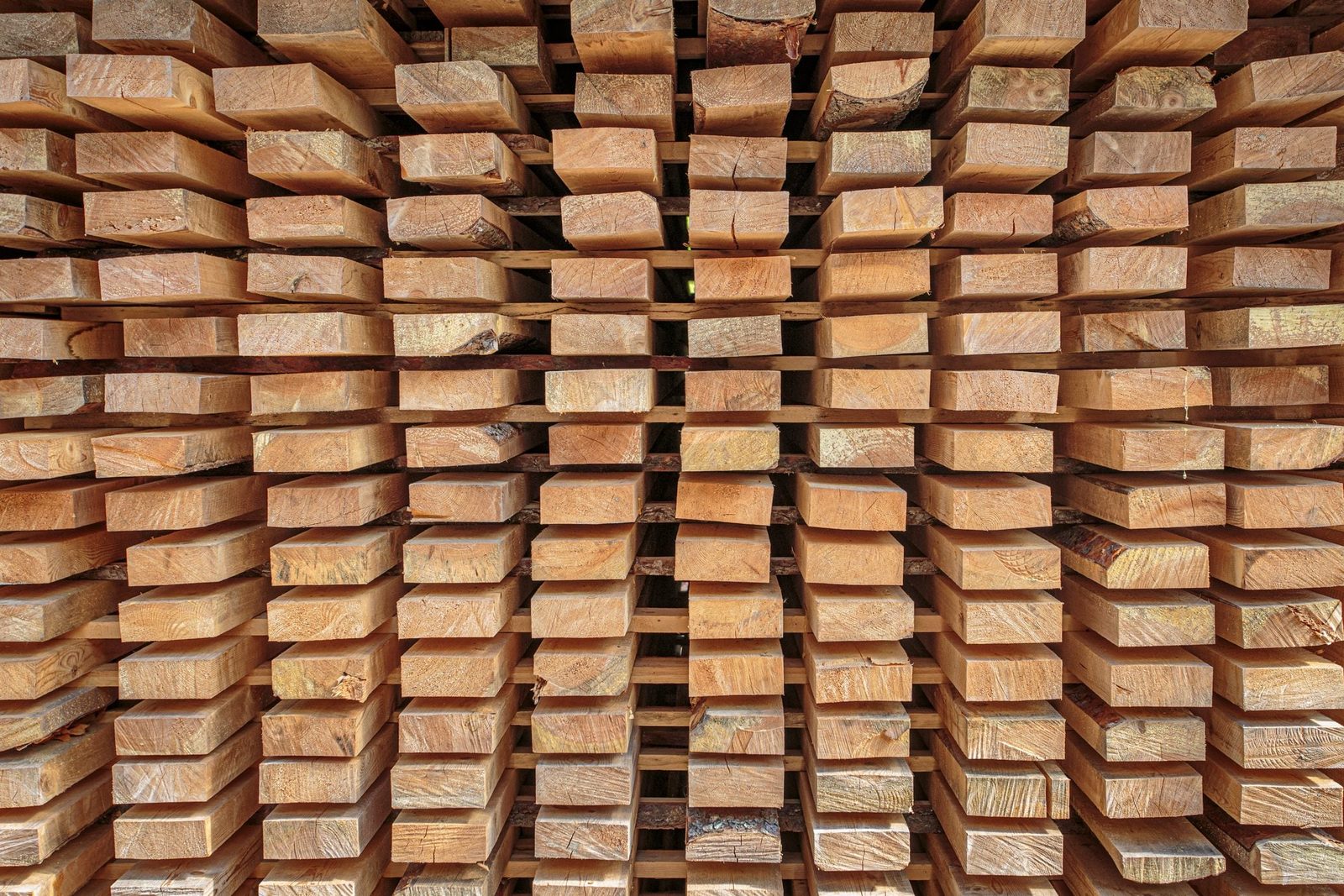 Stacks of wooden planks are neatly arranged, lying horizontally and vertically, showcasing varied textures and colors in a structured, order