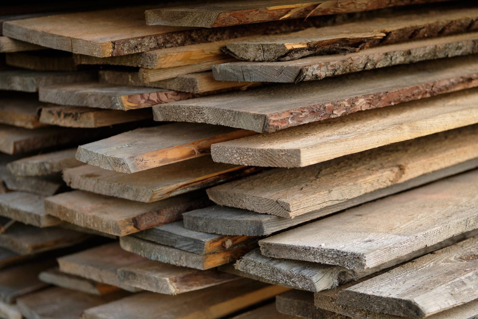 Wooden planks are stacked orderly, showcasing various textures and colors, in a storage area that suggests preparation for construction or c