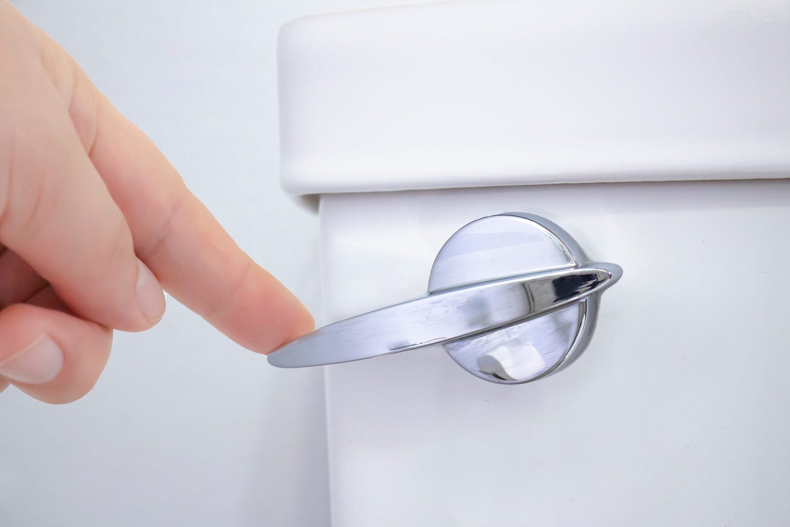 A person flushing a toilet in a washroom of a residential home bathroom.