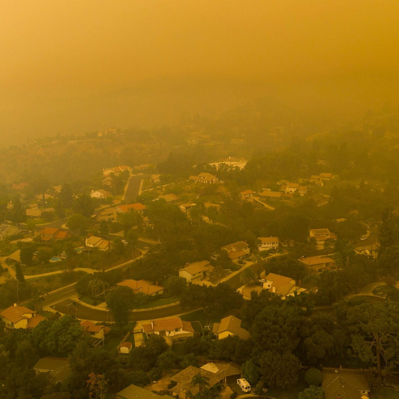Aerial view of suburban homes with thick, orange wildfire smoke in the air