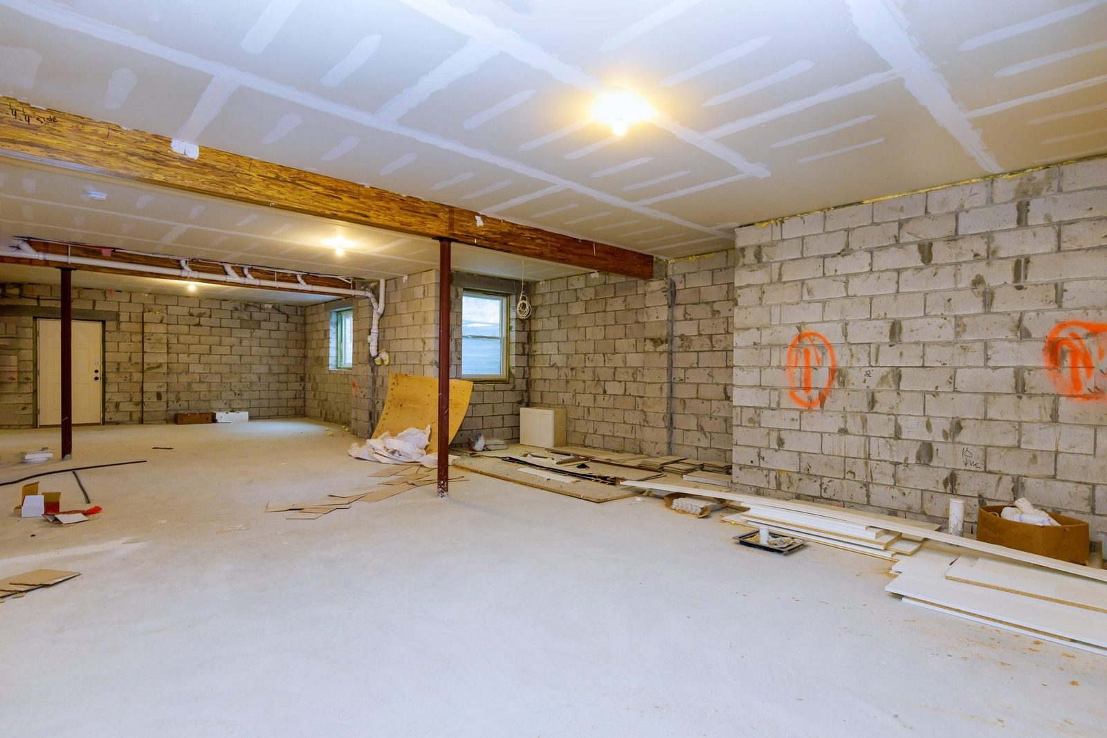 An unfinished basement features exposed block walls, scattered construction materials, and bare concrete floors, illuminated by ceiling ligh