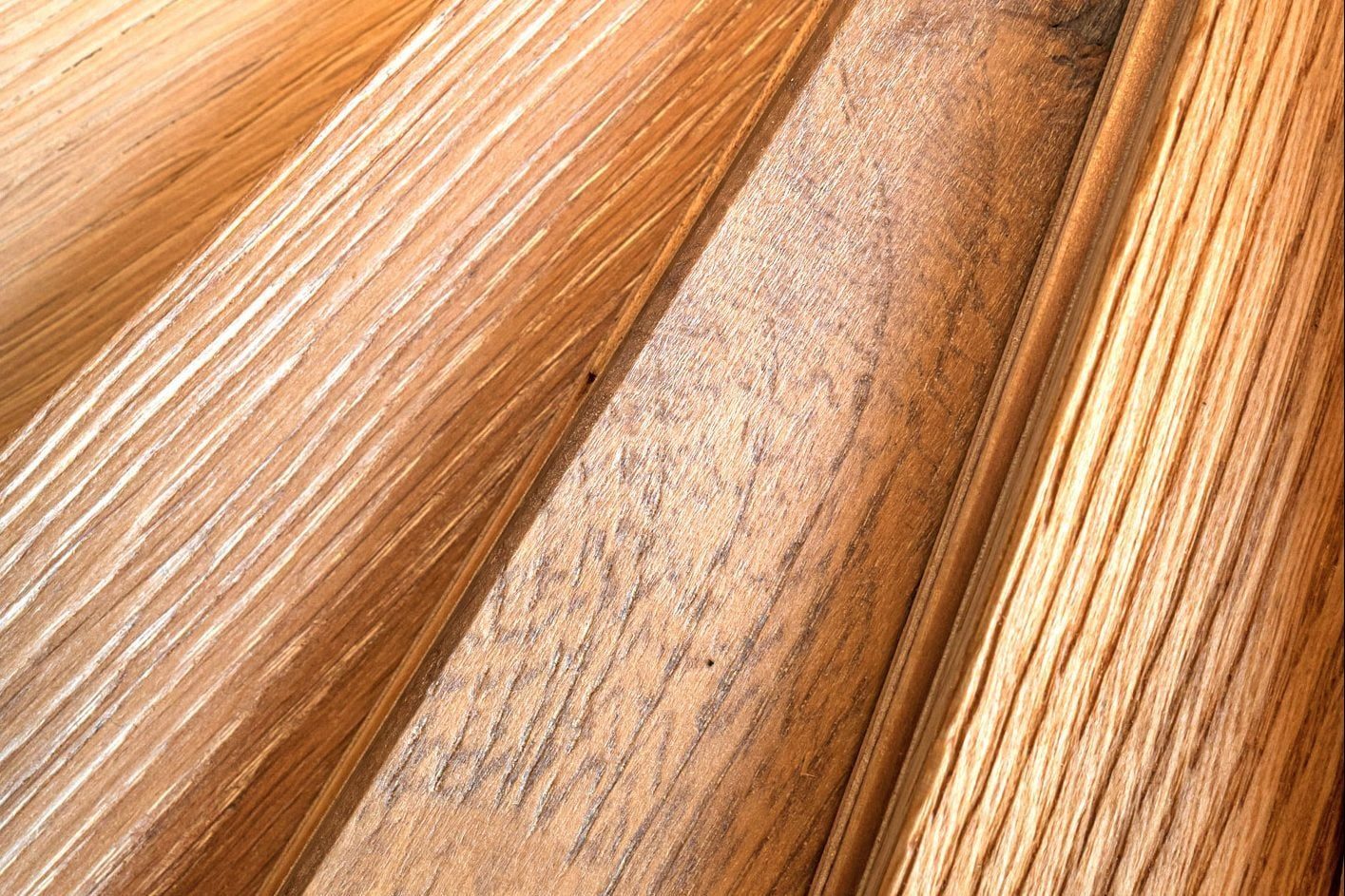 Wooden planks lie at angles, showcasing varied textures and shades, reflecting light in a warm, natural setting that highlights their grain