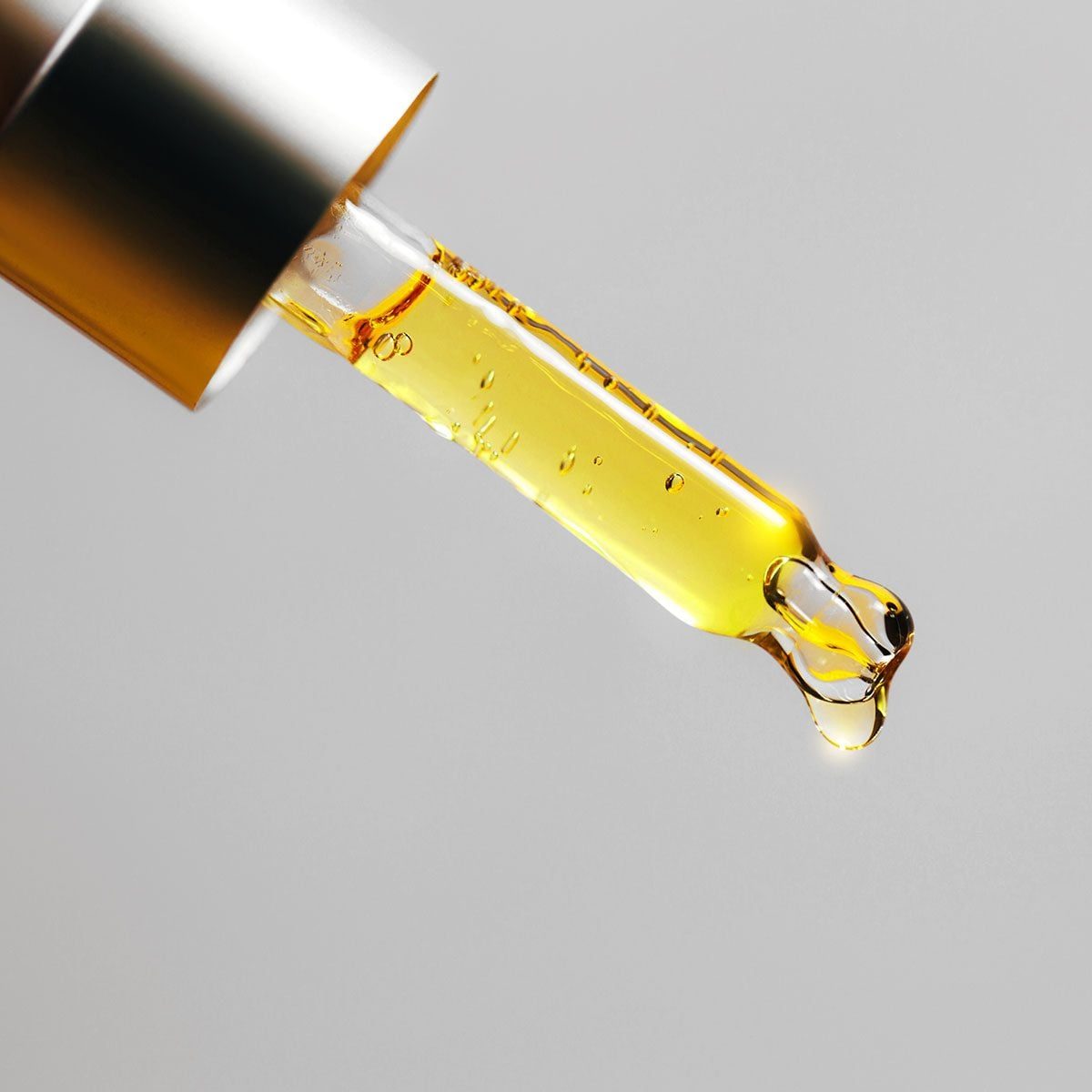A dropper filled with golden liquid is poised above, releasing a droplet against a plain, light backdrop, suggesting a skincare or essential
