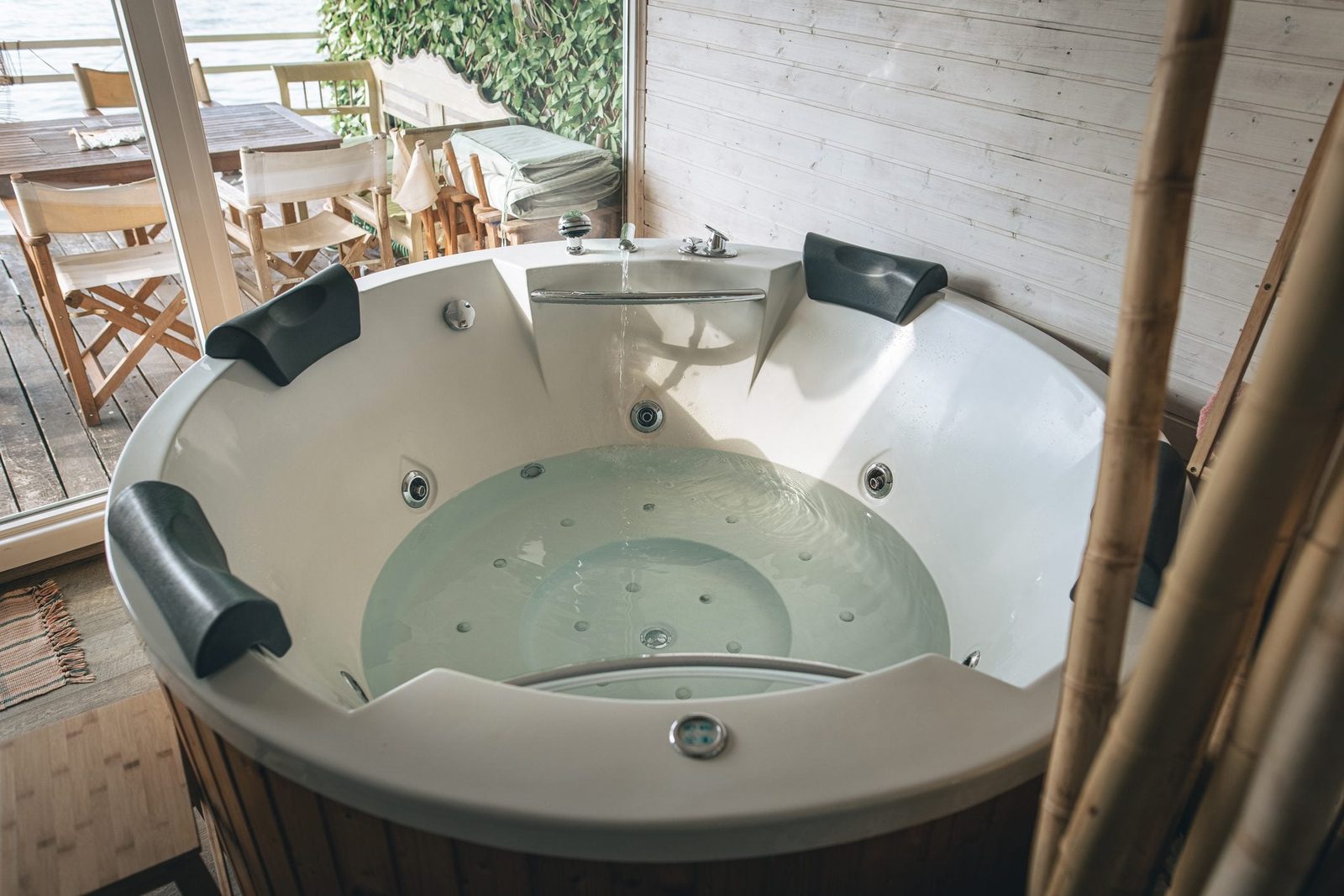 A circular hot tub with water bubbles sits in a wooden space, surrounded by plants and furniture, creating a relaxing atmosphere.