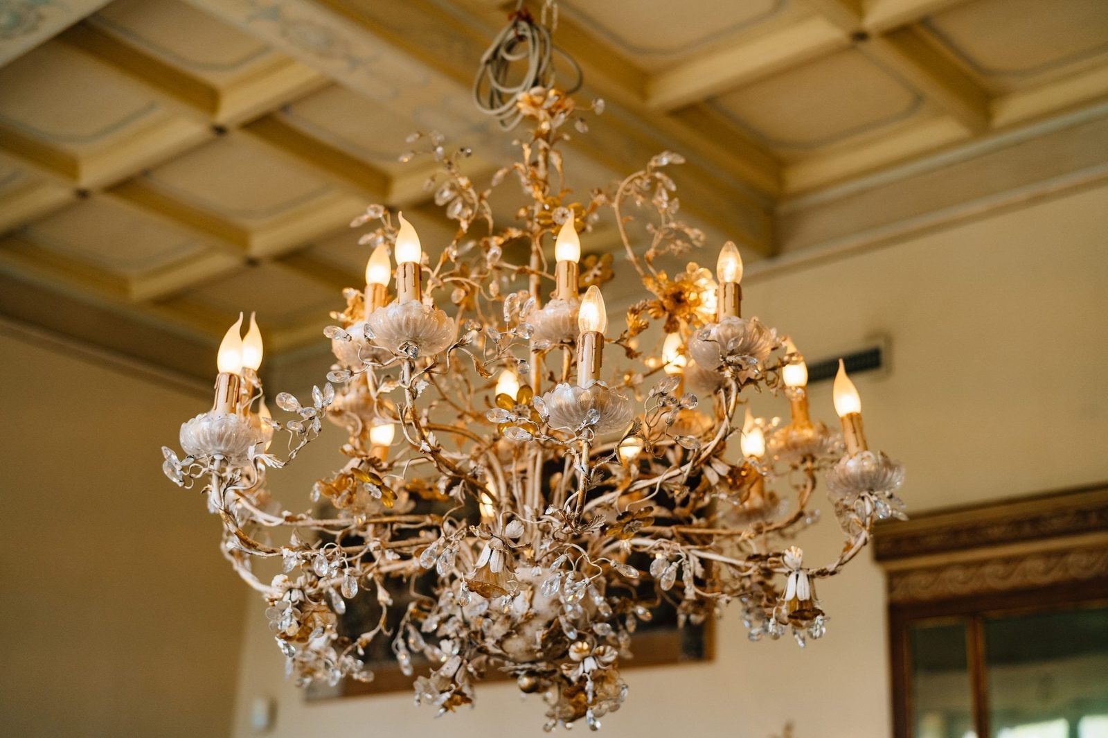 A decorative chandelier hangs from the ceiling, illuminating the room with warm, soft light, surrounded by neutral-colored walls and classic