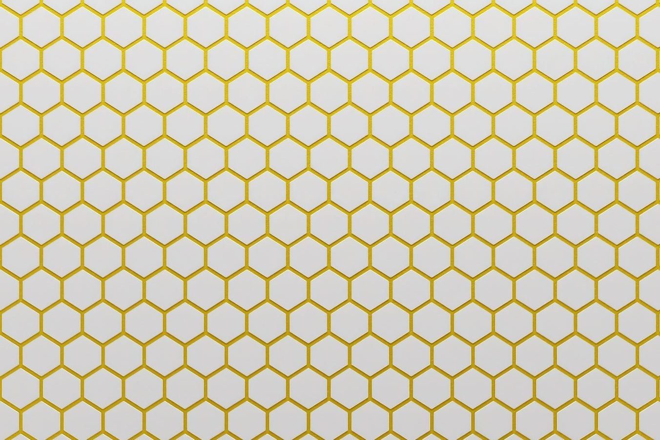 A repetitive pattern of yellow hexagons is arranged on a white background, creating a grid-like design reminiscent of a honeycomb structure.