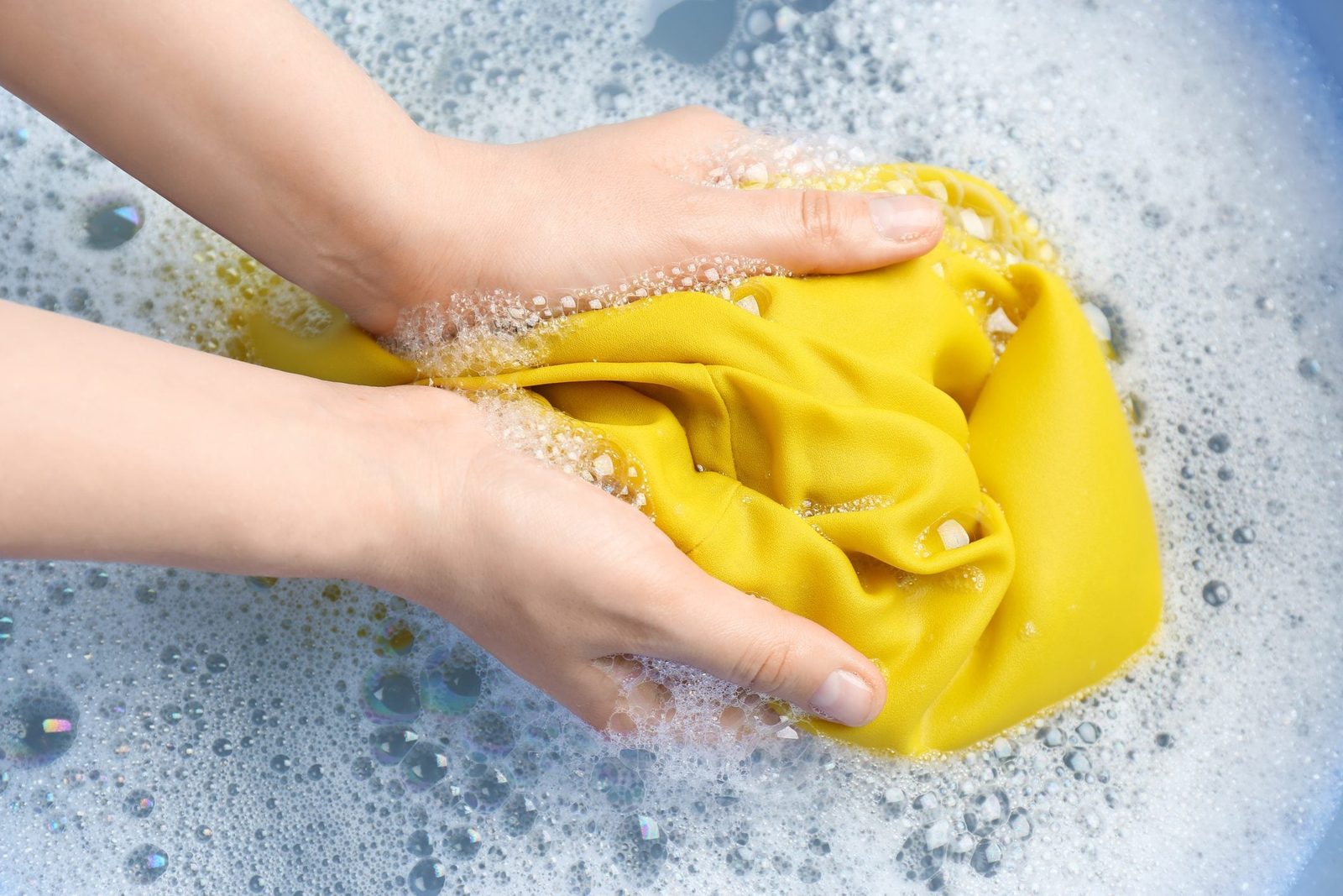 Top view of woman hand washing color clothing in suds, closeup