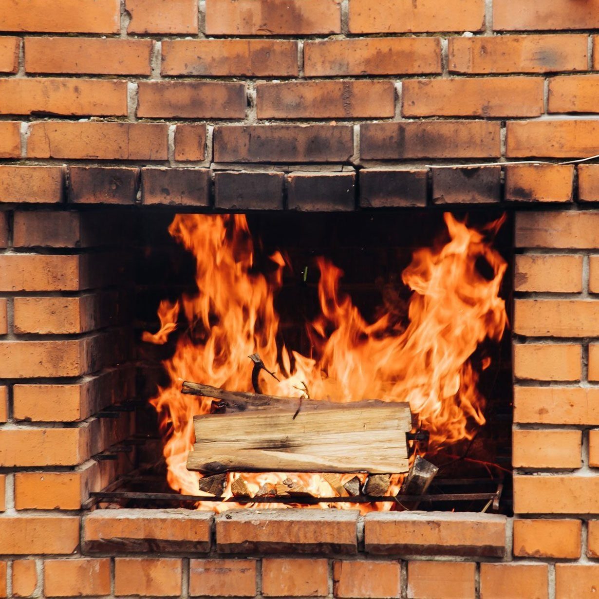 A glowing fire burns brightly in a brick fireplace, with flames dancing around a log resting on a bed of glowing embers.