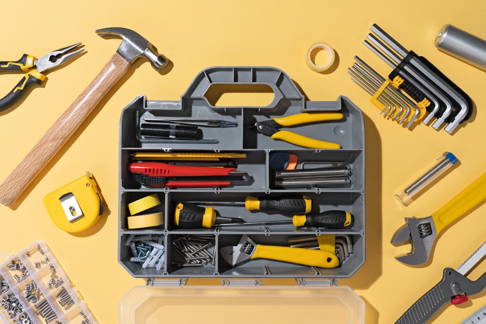 A toolbox is organized with various tools, including a hammer, screwdrivers, and pliers, placed on a yellow surface.