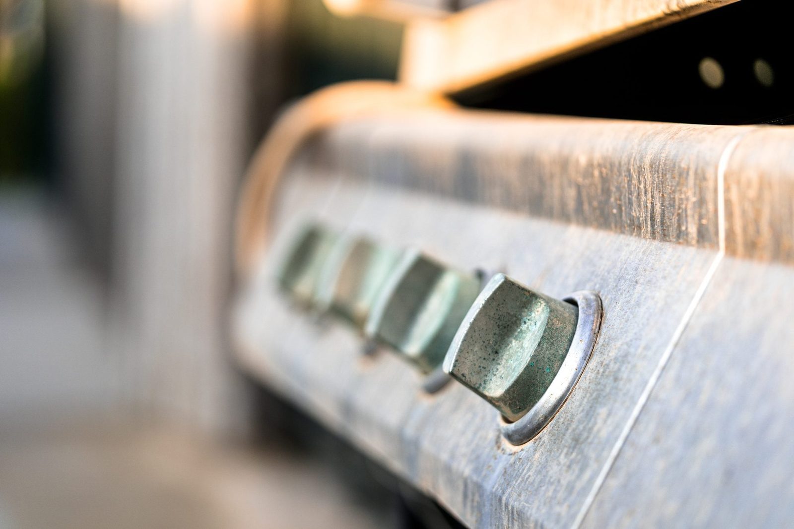 A close-up of metal knobs on a grill, suggesting the action of adjusting heat settings in an outdoor cooking environment.