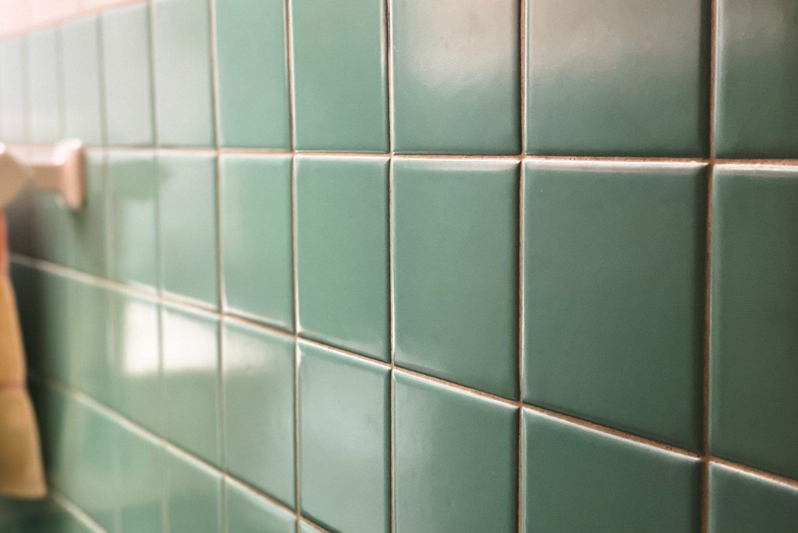 Green ceramic tiles line a wall, providing a glossy surface in a bathroom setting, with soft lighting enhancing their color and texture.