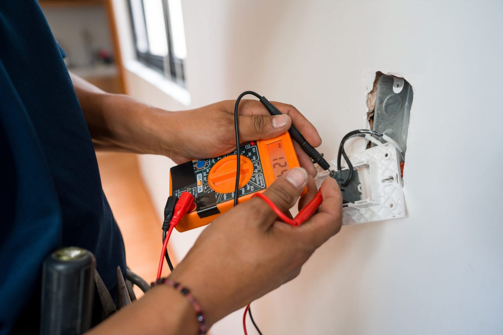 A person is measuring voltage with a multimeter on an electrical outlet, surrounded by a clean, well-lit indoor environment.