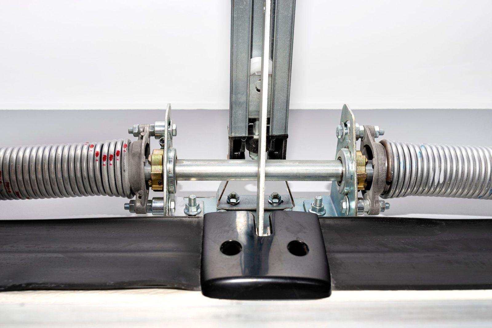 A spring and pulley mechanism is positioned centrally, with metal components securely fastened on a black base, set against a plain white ba
