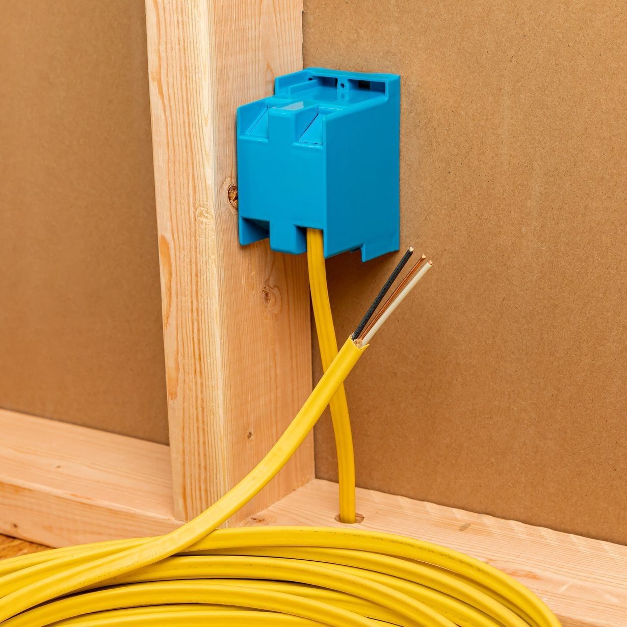 A blue electrical junction box is mounted on a wall, with yellow wires emerging from it and coiled along a wooden floor.