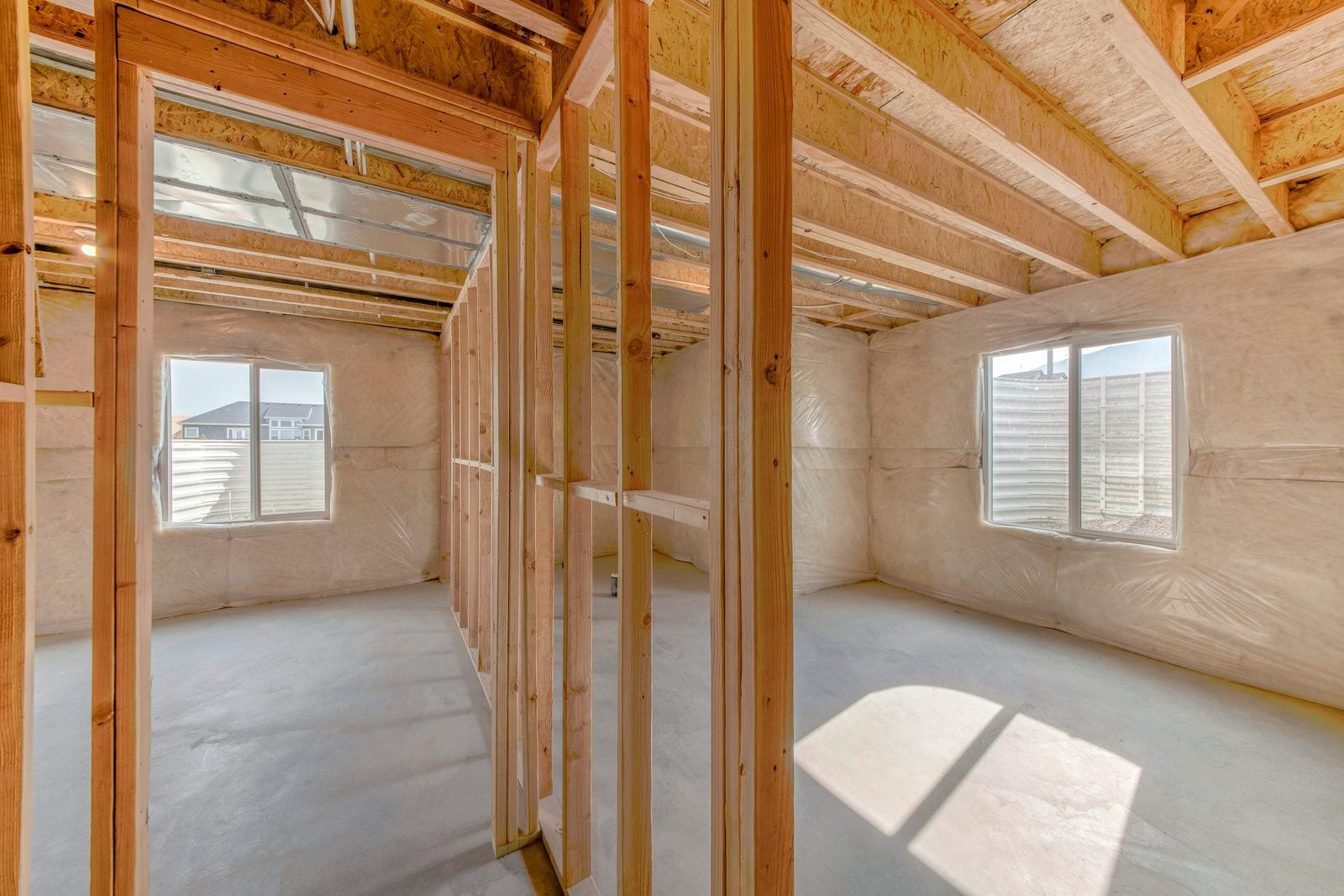 Framed walls stand in an unfinished interior space, with sunlight streaming through windows and a concrete floor, suggesting ongoing constru