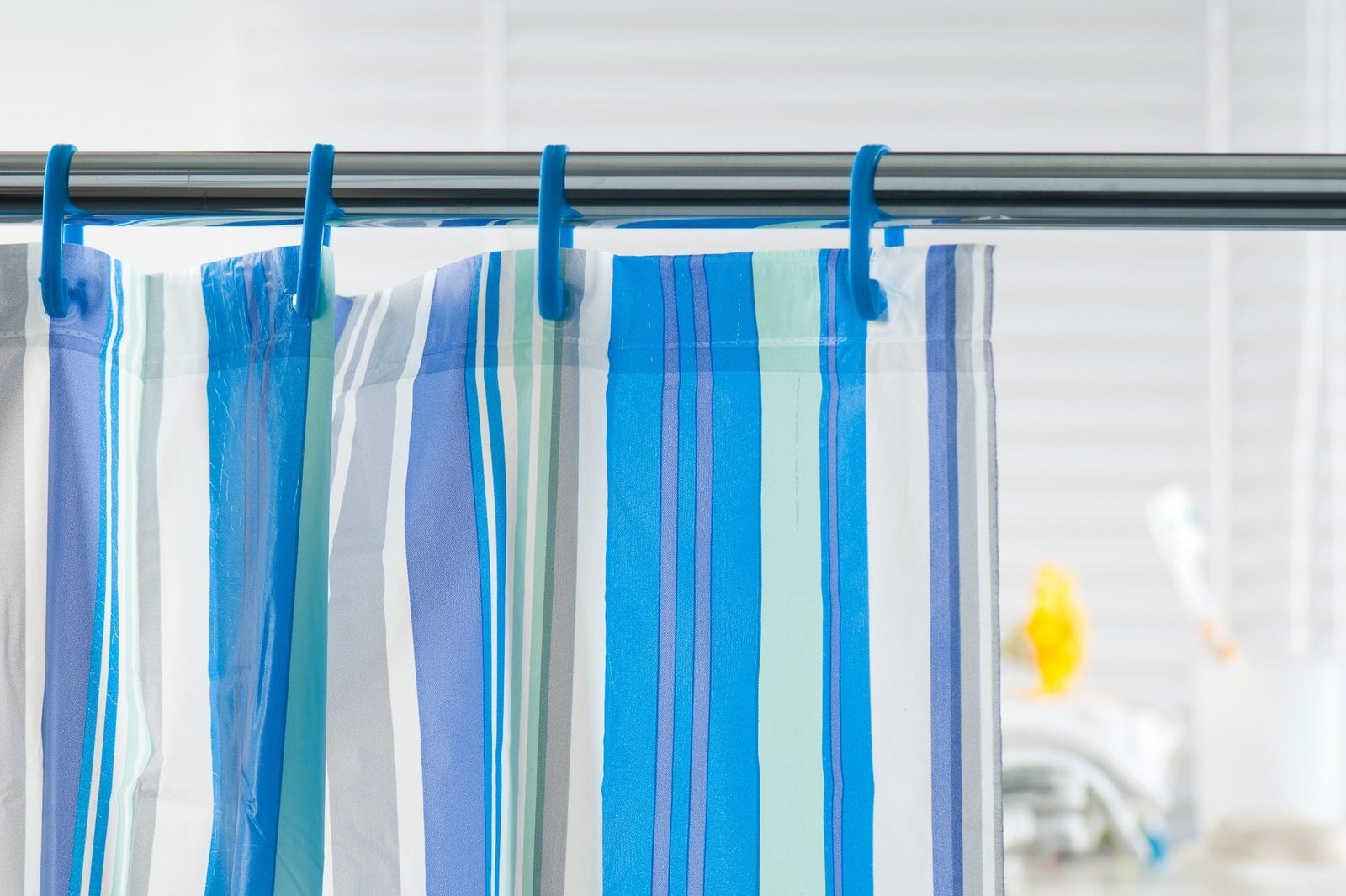 Striped shower curtain hangs on a rod, providing privacy in a bright bathroom space with blurred objects in the background.