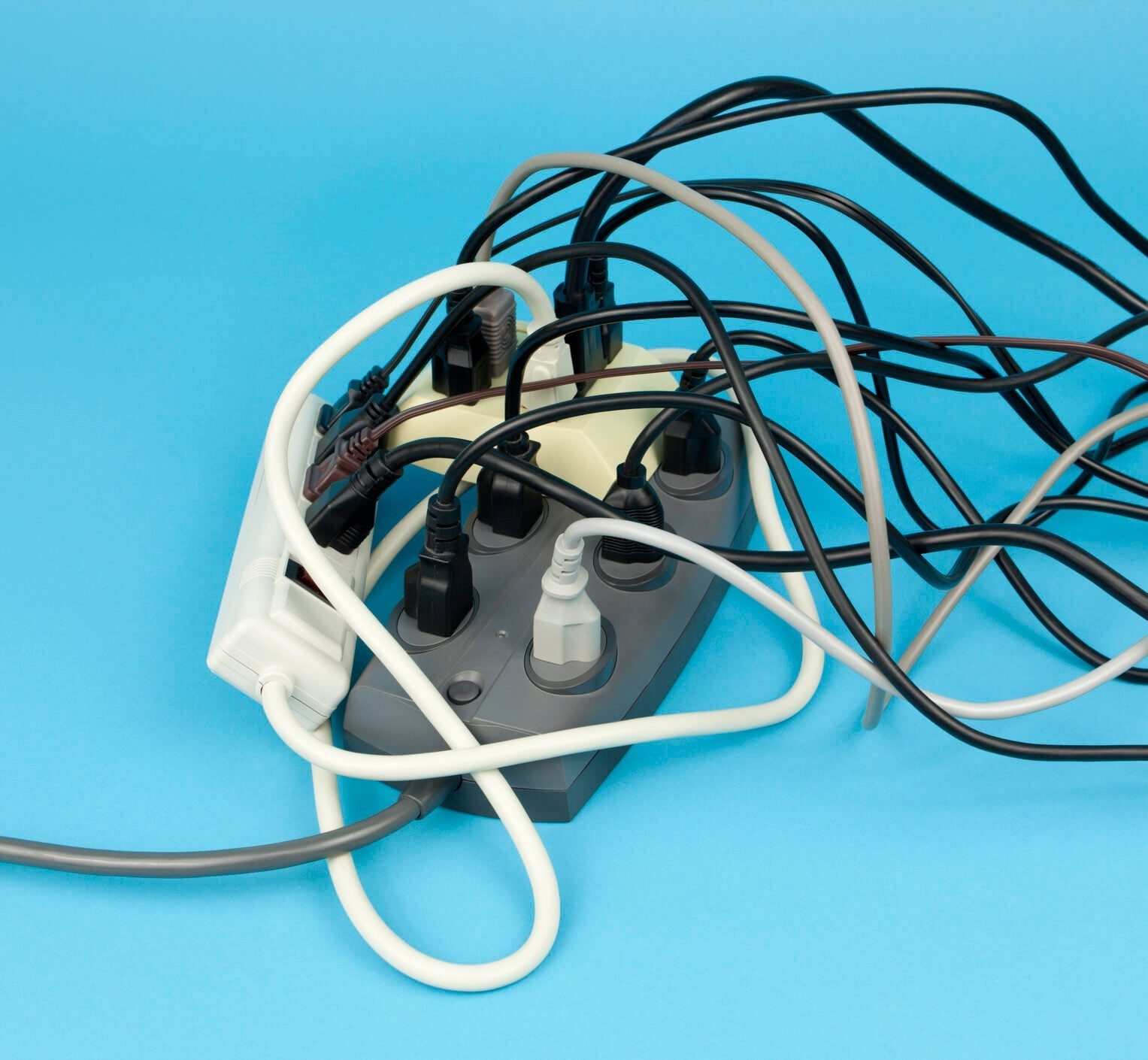 Multiple extension cords and surge protectors plugged into each other with tangled cords on a blue background