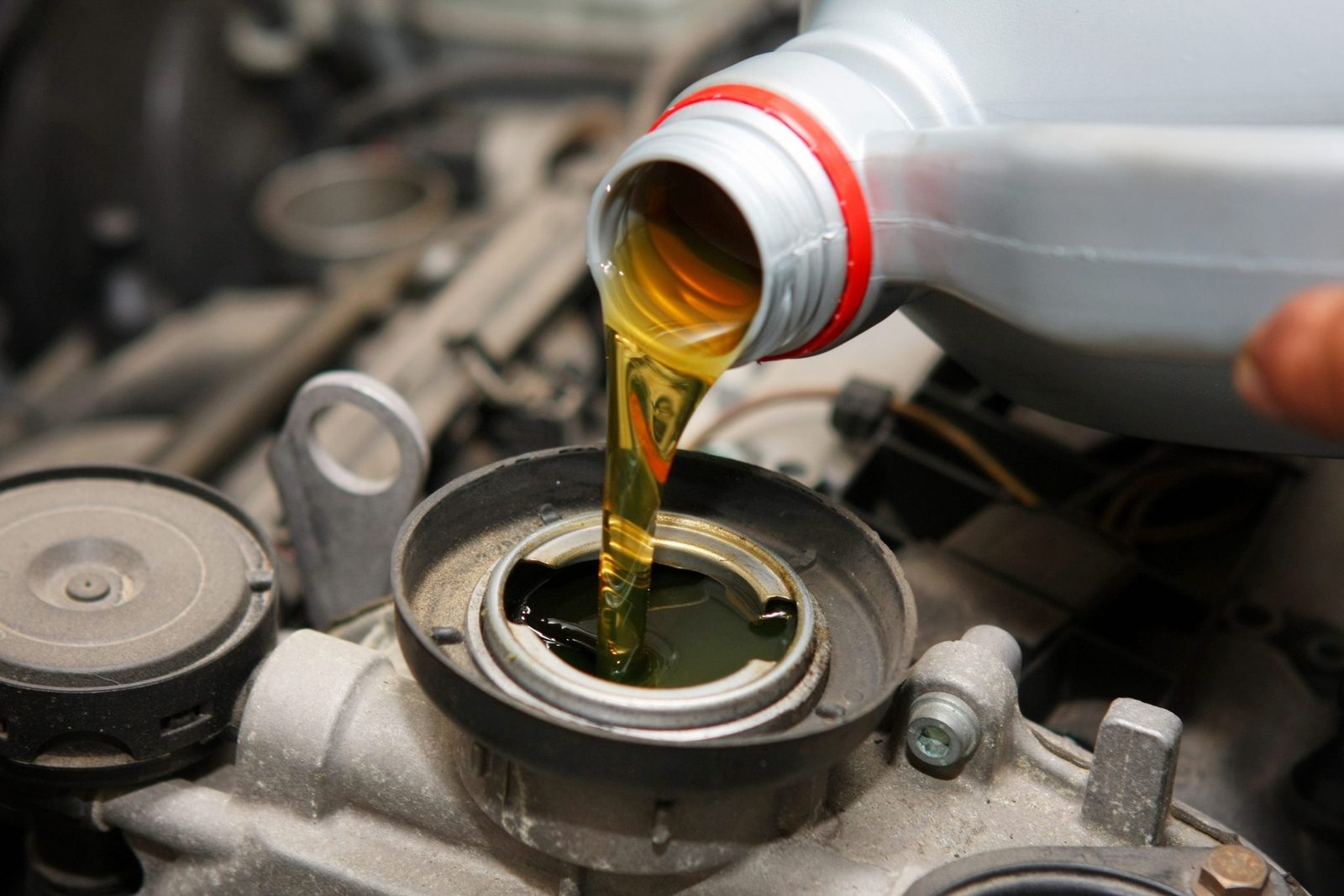 A bottle pours golden oil into an engine’s oil reservoir, surrounded by mechanical components in a vehicle’s engine bay.