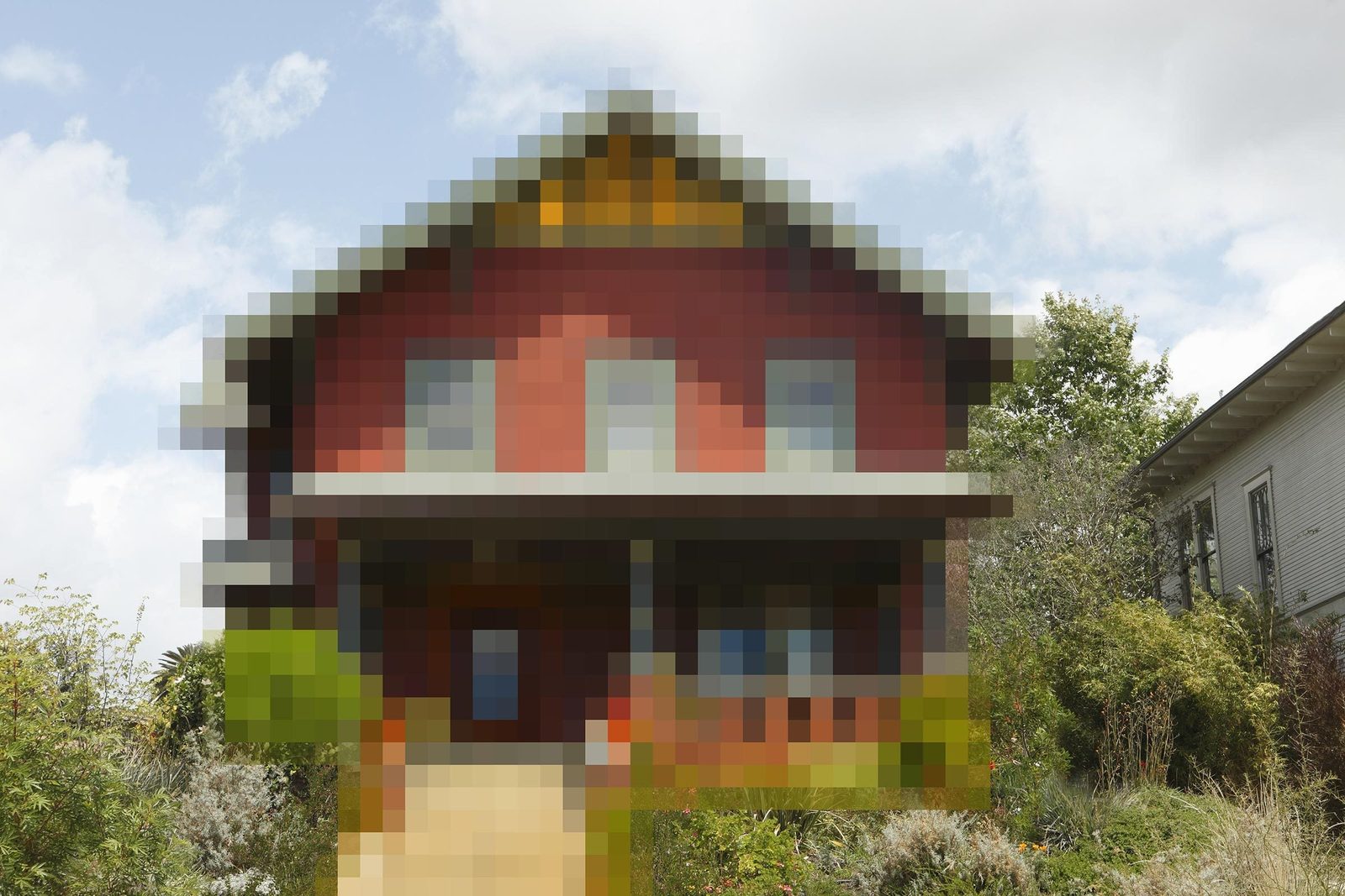 A red house stands with a front porch, surrounded by greenery and trees under a partly cloudy sky.