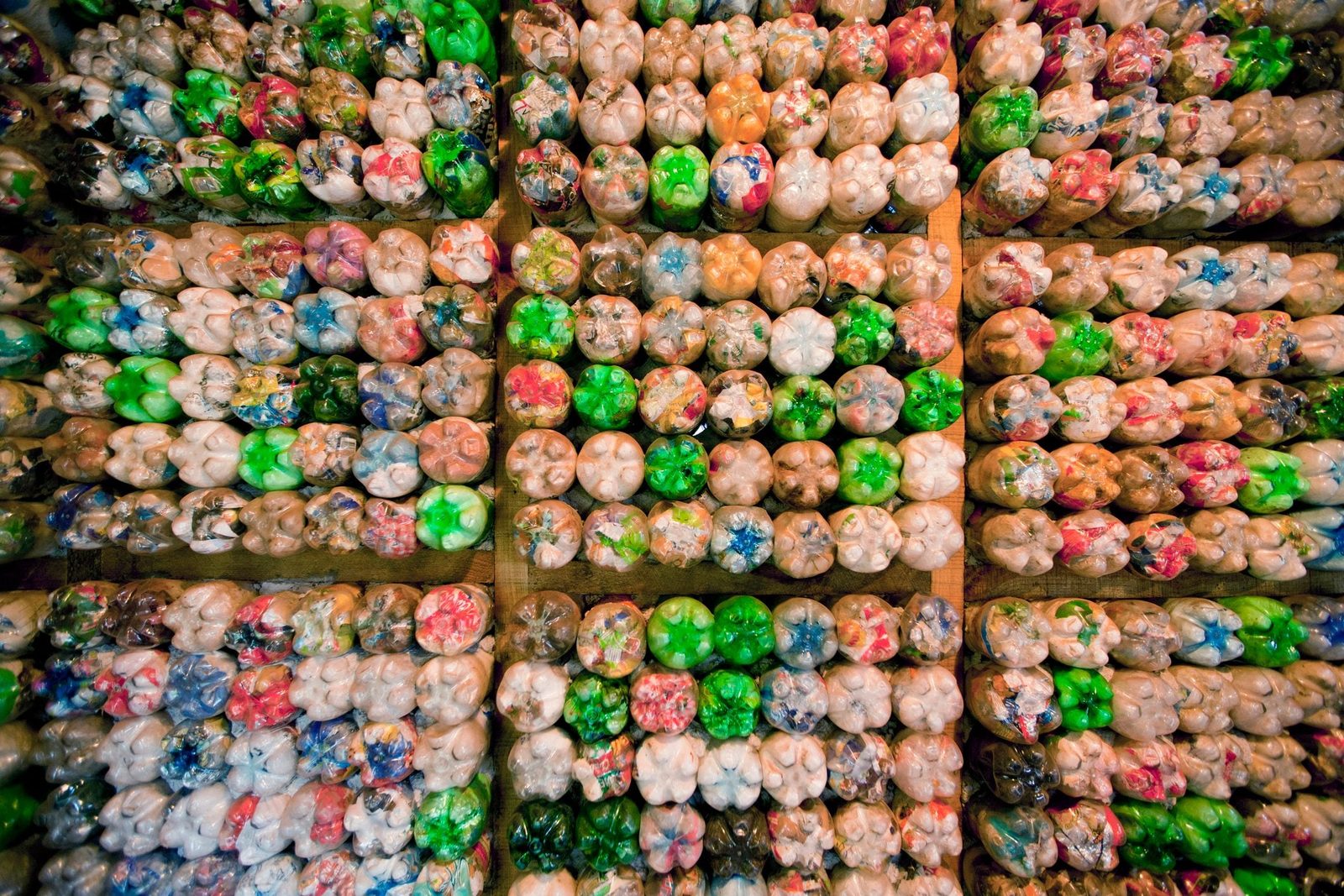 Rows of colorful plastic bottles are organized neatly, displaying a variety of hues, stacked on wooden surfaces in a structured arrangement.