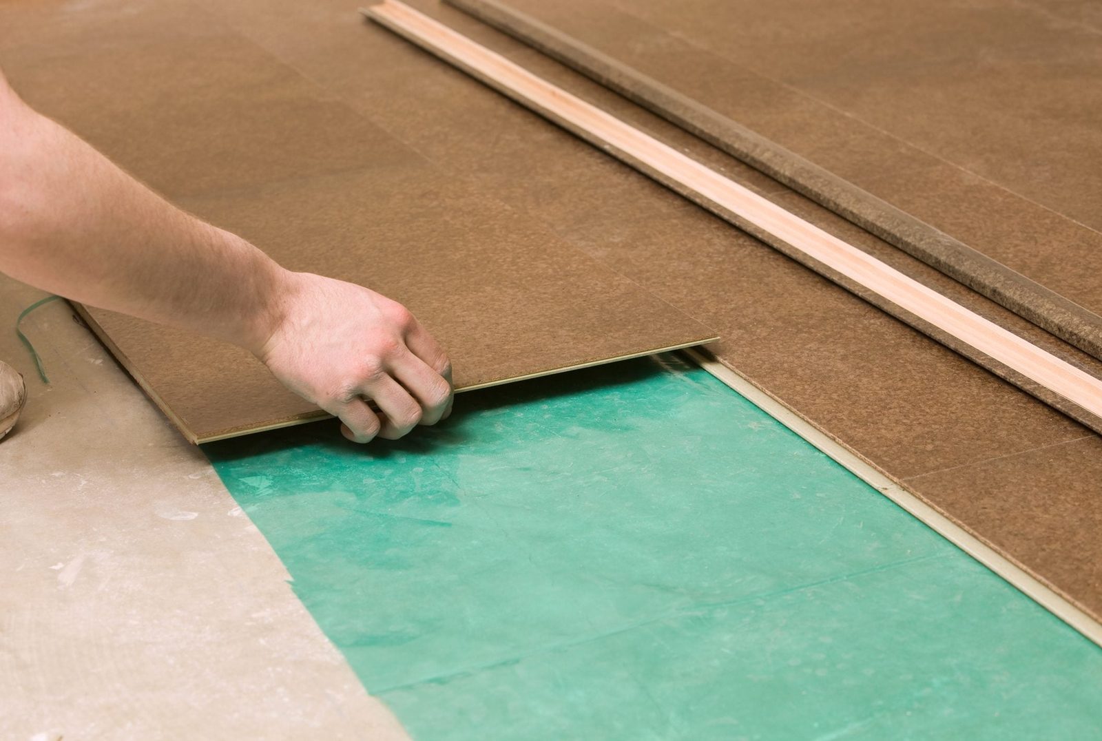 A hand places a flooring panel onto a green protective sheet, surrounded by additional panels on a flat surface, indicating a flooring insta