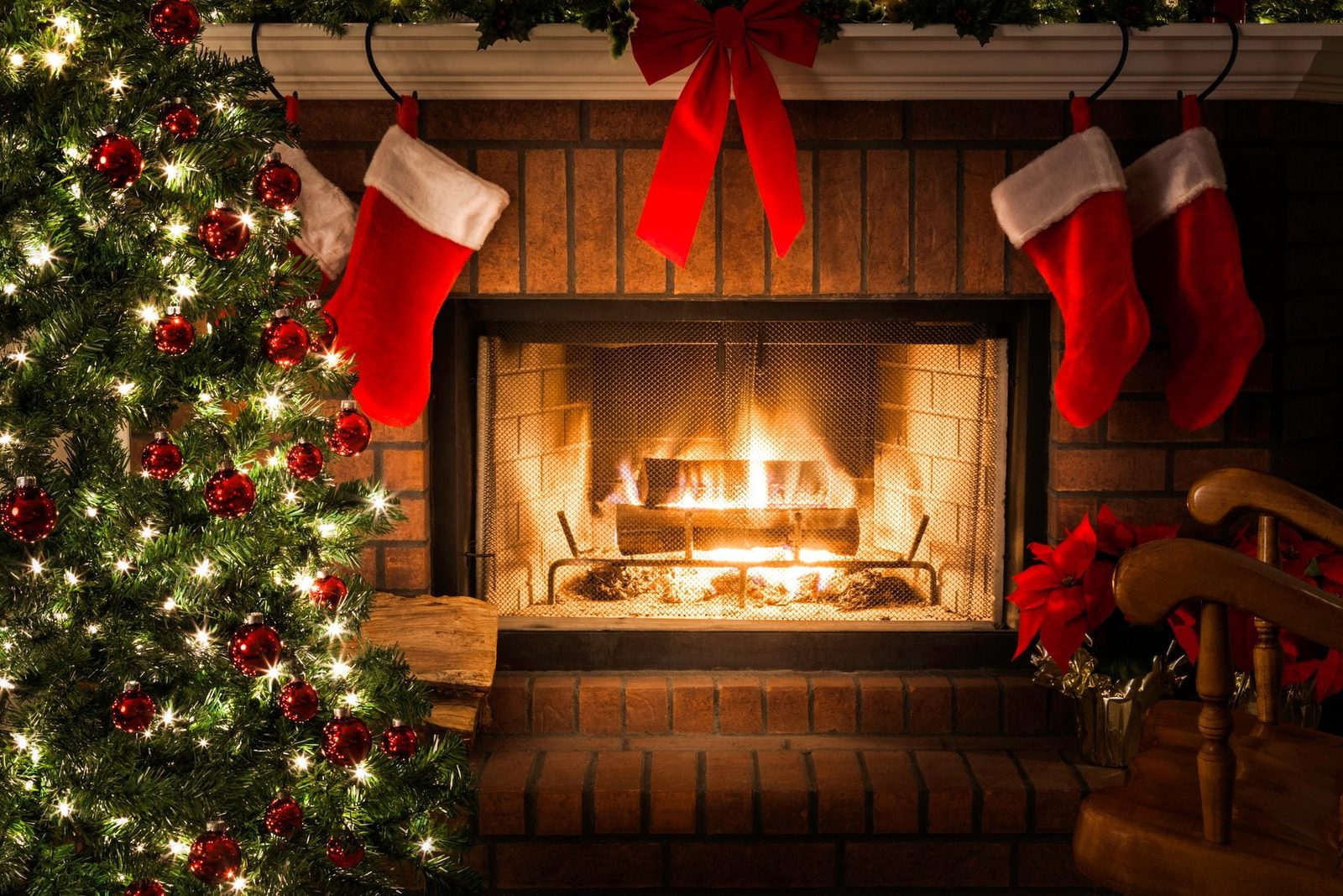 A decorated Christmas tree stands beside a glowing fireplace, with red stockings hanging above, creating a cozy festive atmosphere.