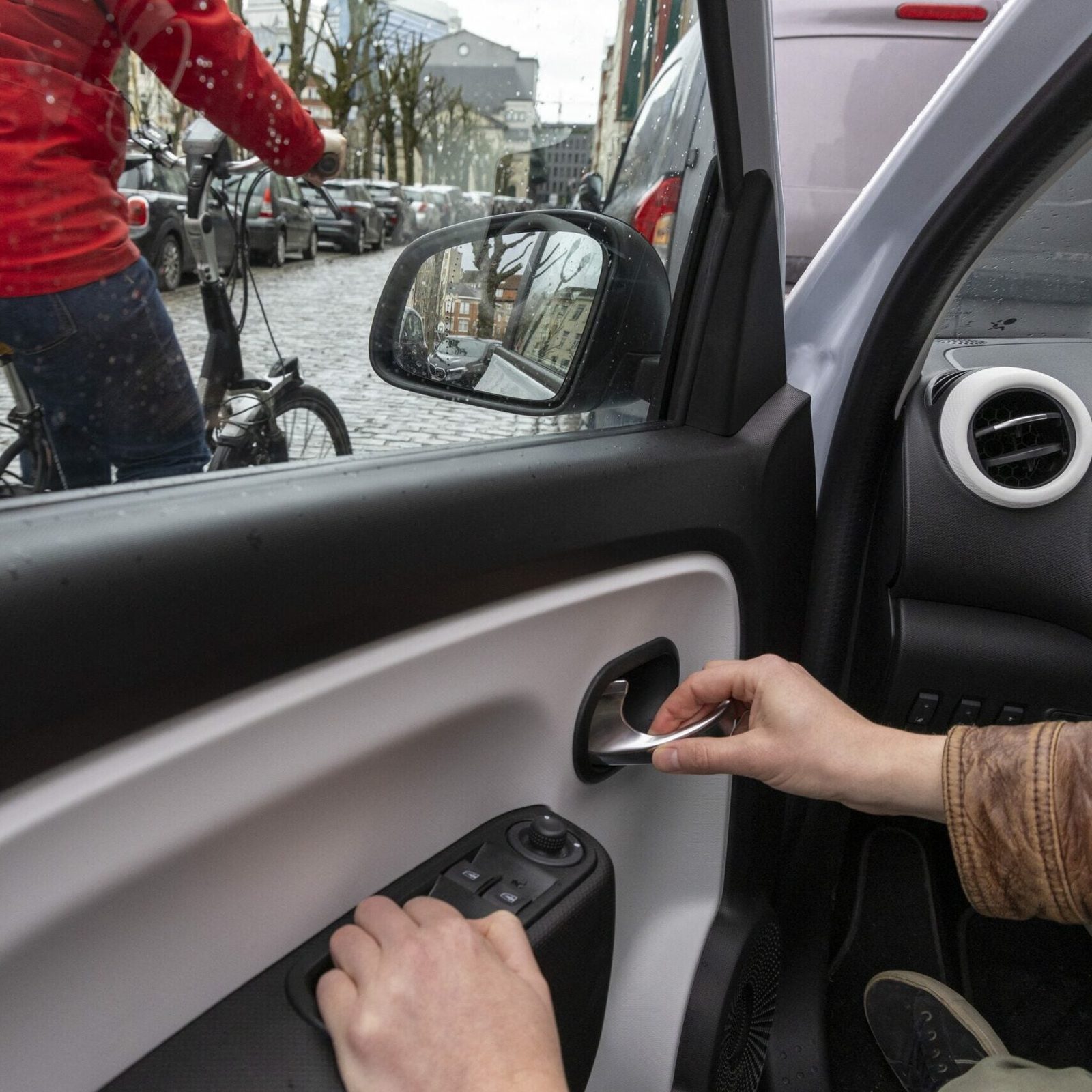 A car driver opens the door of his car with the 'Dutch reach' method, making the driver turn and look into the rear view mirror and over the