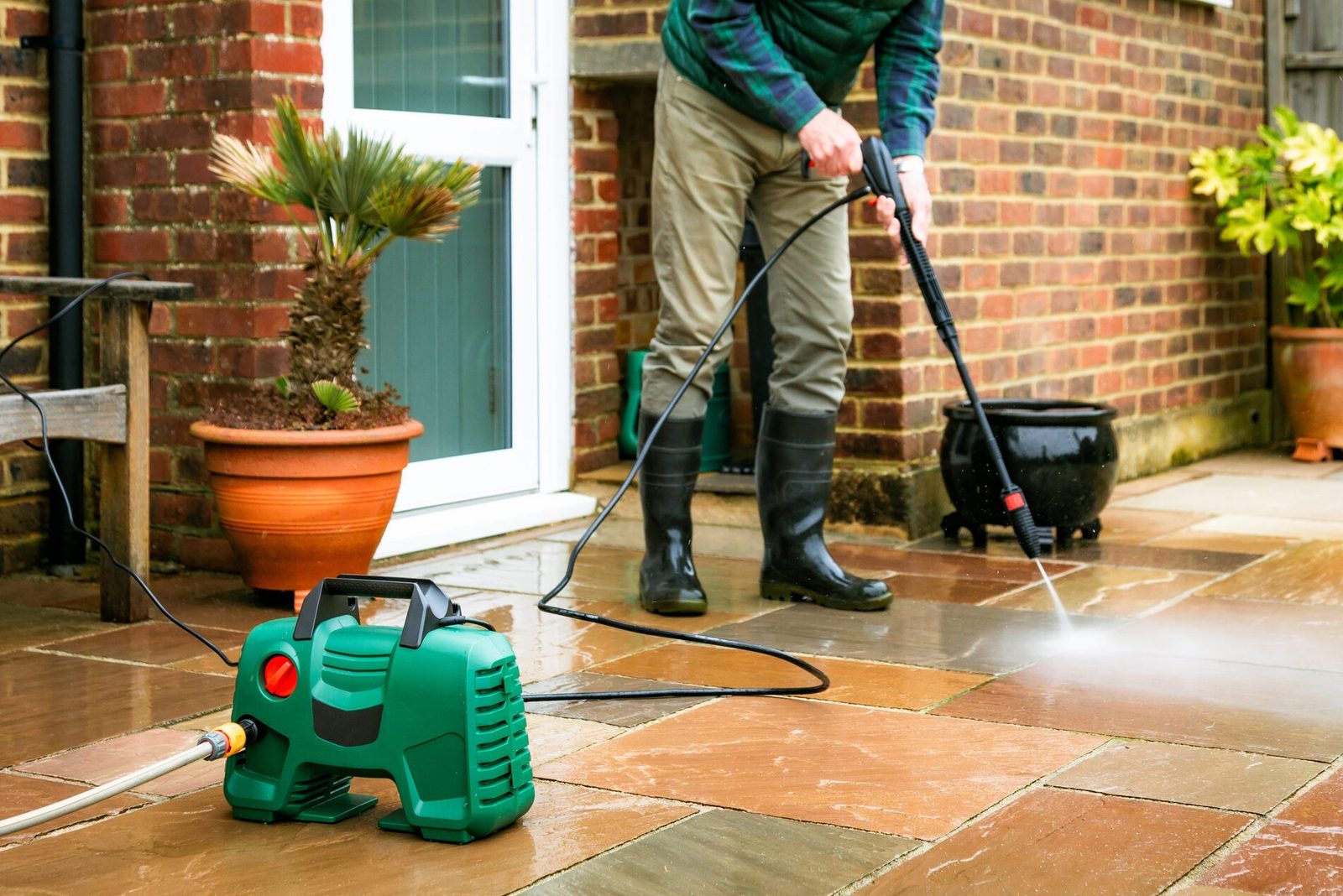 Senior man cleaning patio tiles using pressure washer