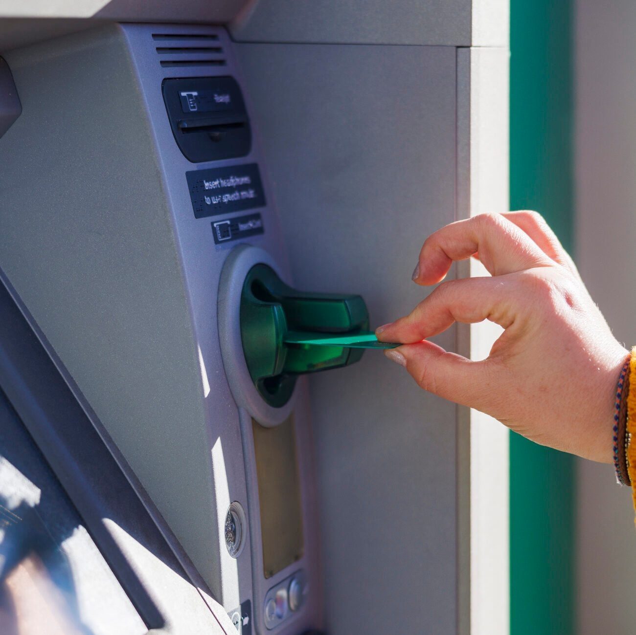 Woman hand inserts green debit card into atm machine skimmer slot