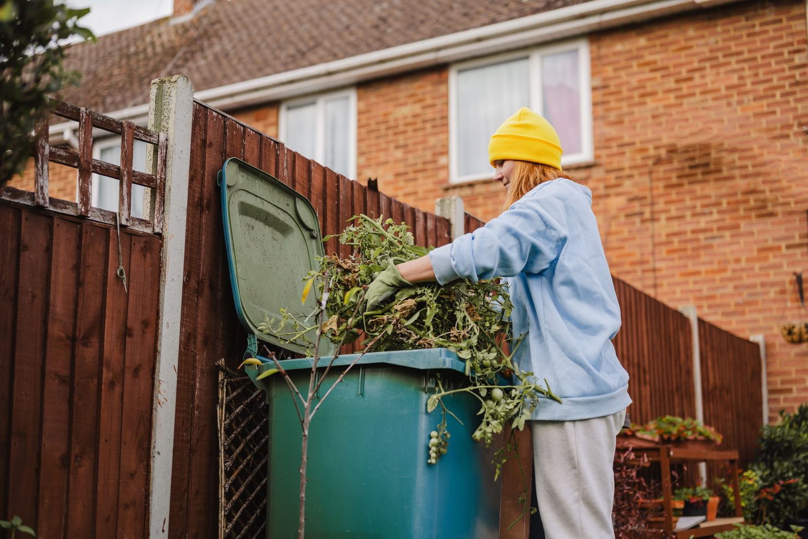 Person disposing garden waste in recycling bin during autumn cleanup
