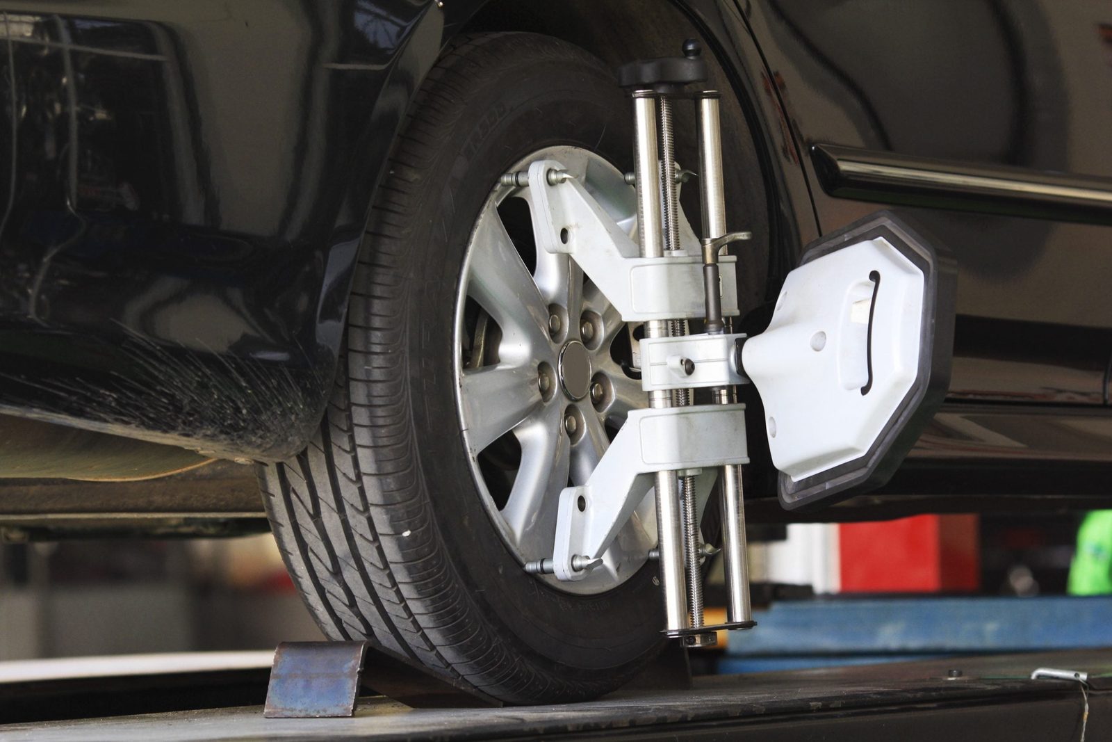 A wheel alignment tool is securely attached to a car tire, positioned on a mechanic's platform in a well-lit garage environment.