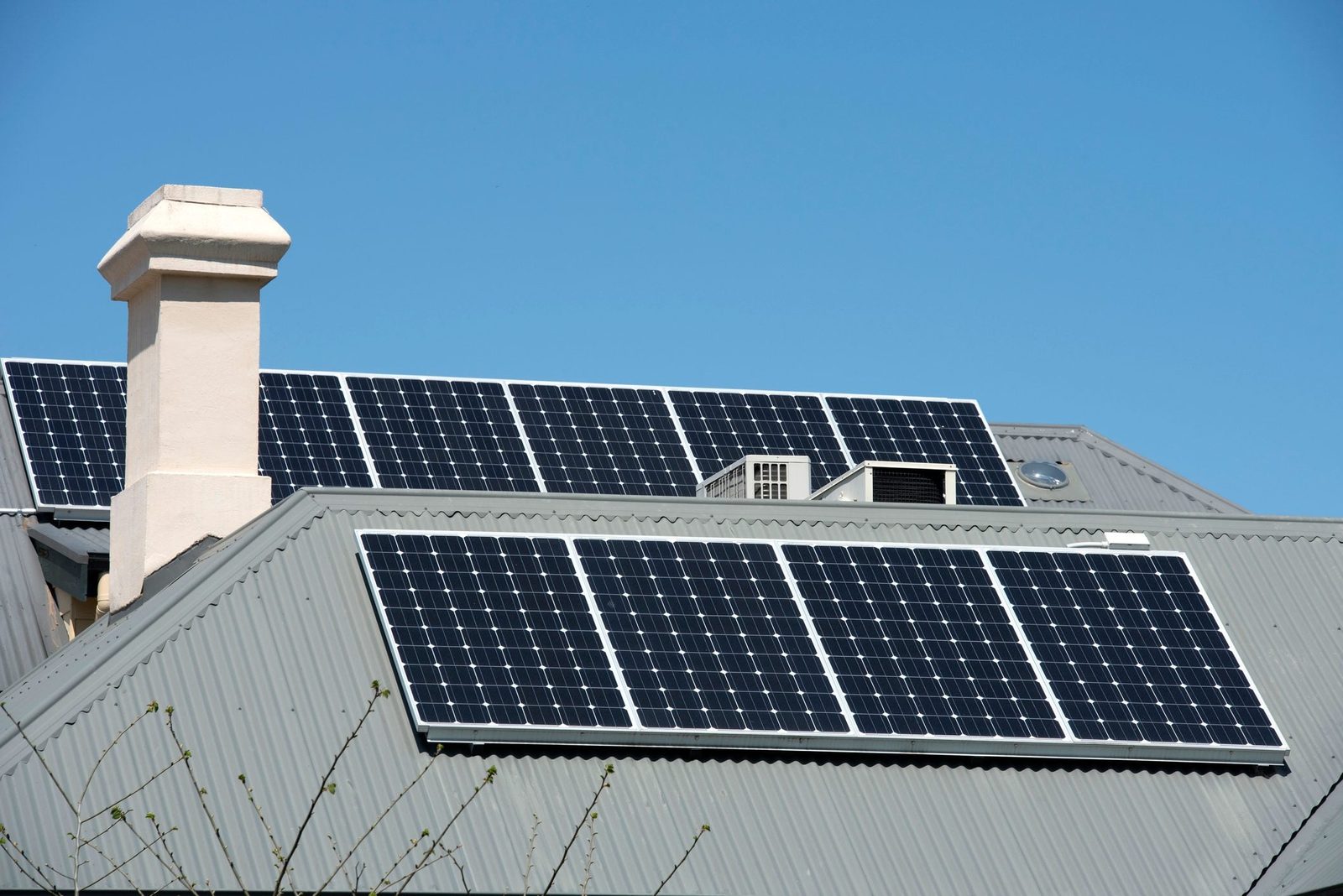 Solar panels occupy a sloped rooftop, capturing sunlight under a clear blue sky, alongside a roof-mounted air conditioning unit and a chimne