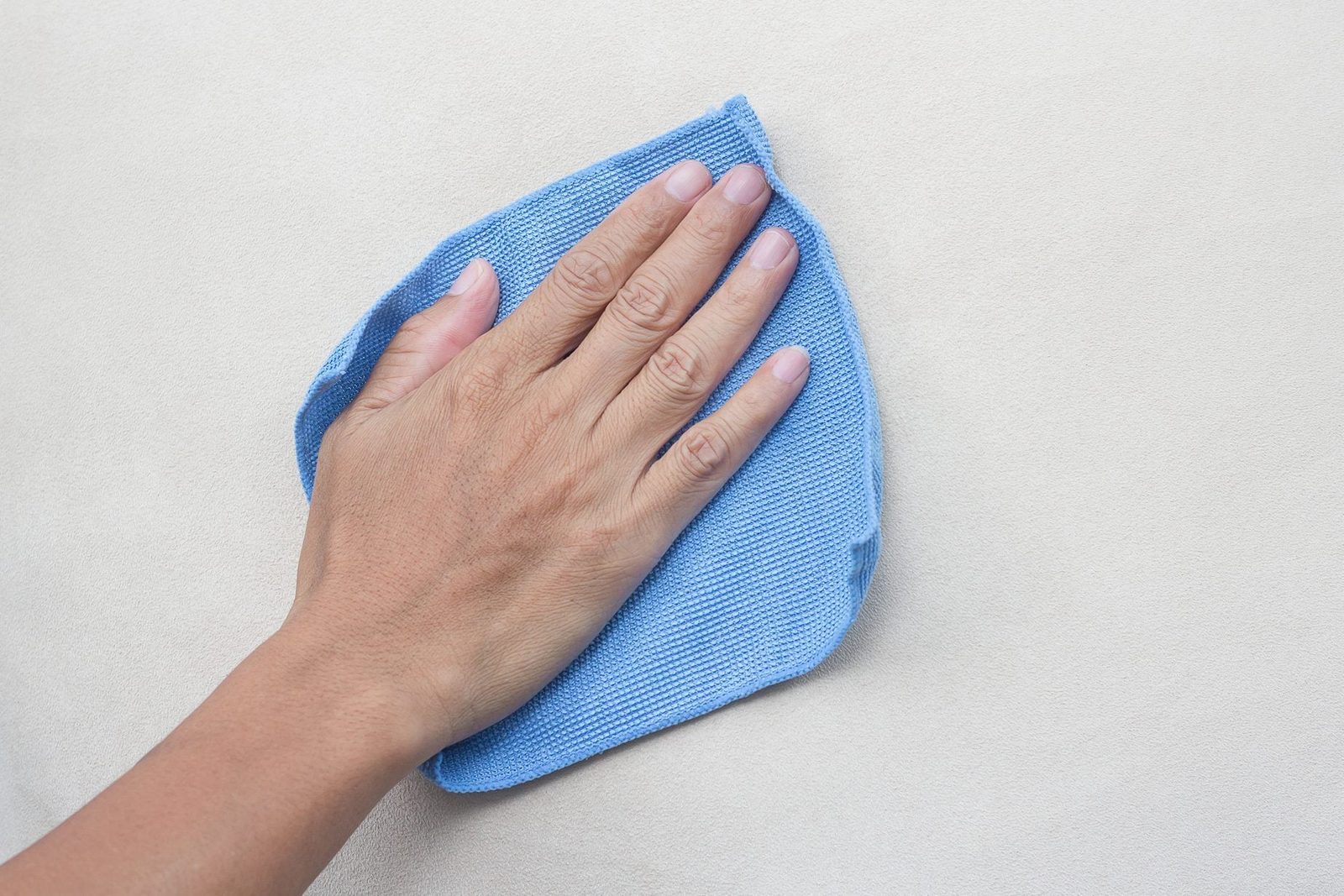 A hand holds a blue cloth, wiping a smooth, light-colored surface to clean it. The environment appears simple and tidy.