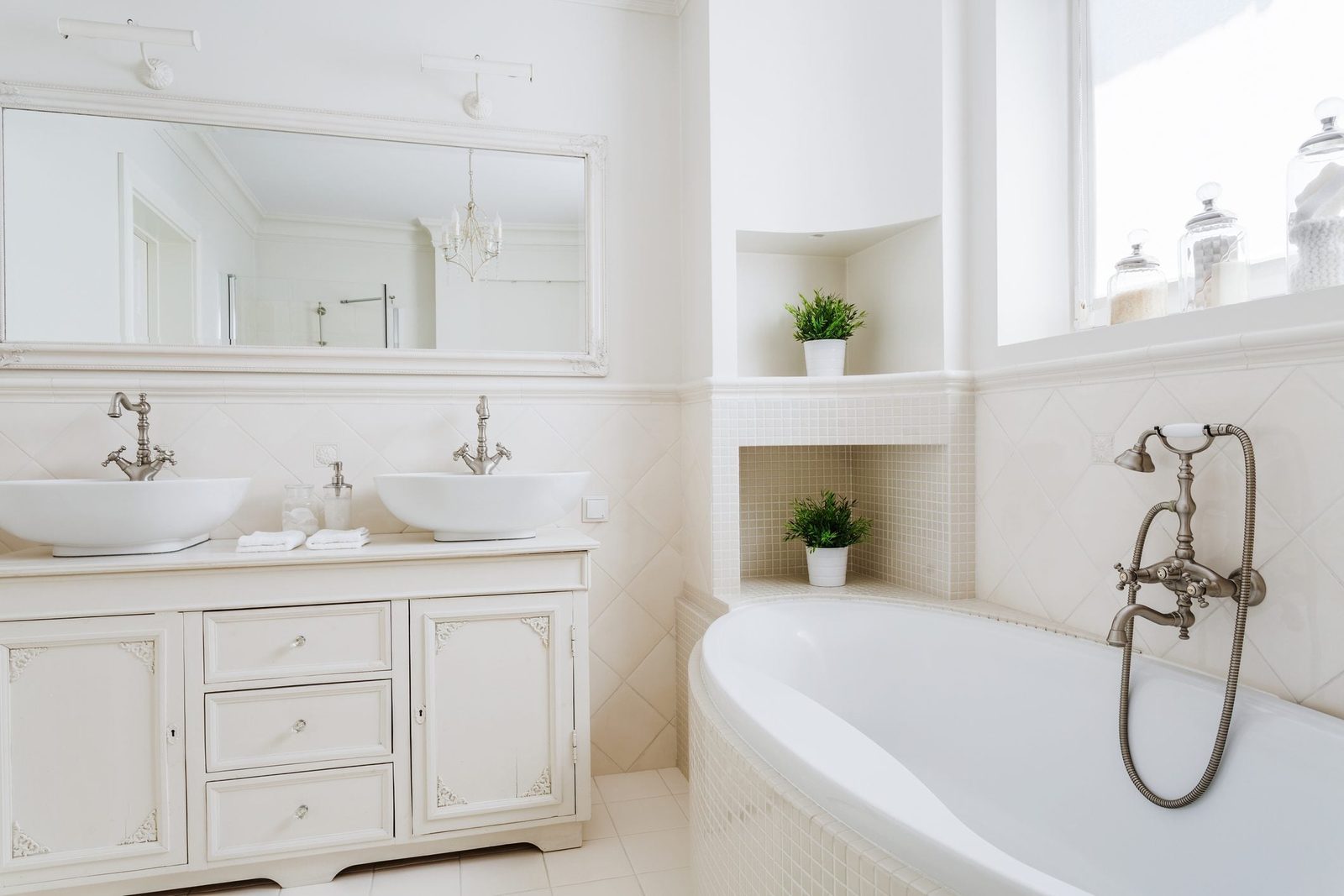 A dual-basin vanity with elegant faucets sits beside a curved bathtub; potted plants accentuate the light, airy bathroom atmosphere with sof
